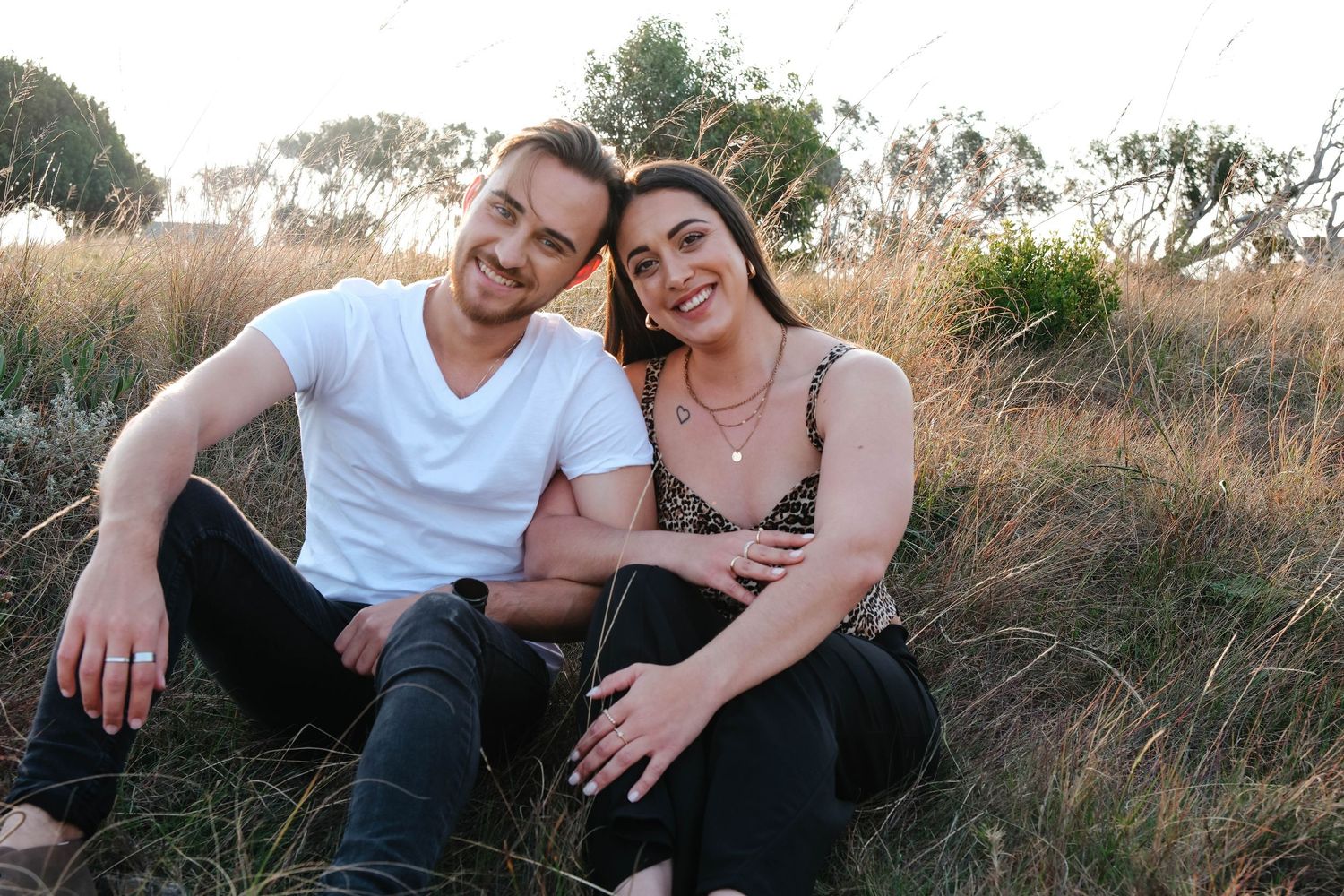 Relaxed couple sitting together on grassy hillside at sunset.