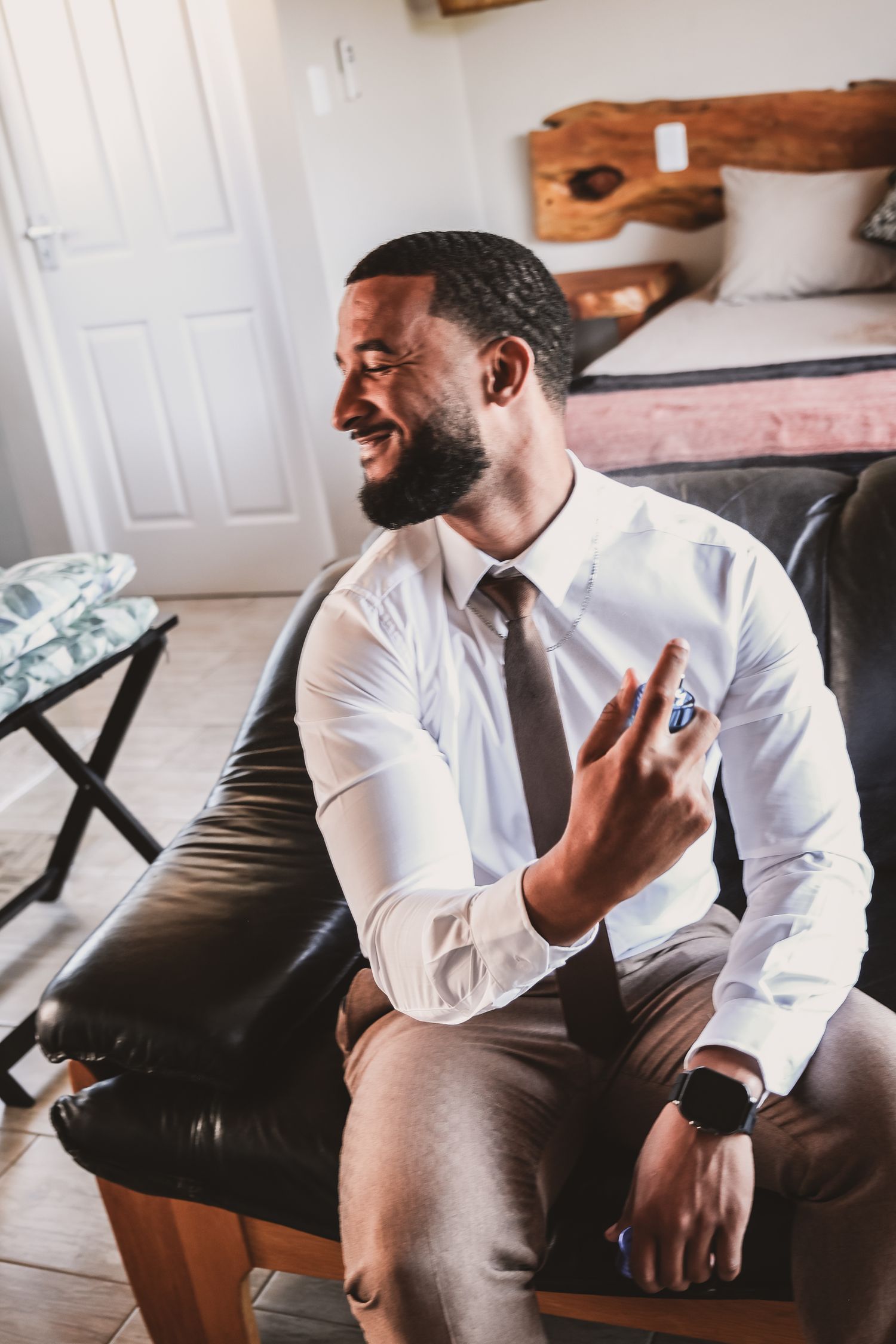 Wedding preparation scene with person in white dress shirt and tie sitting on leather couch.