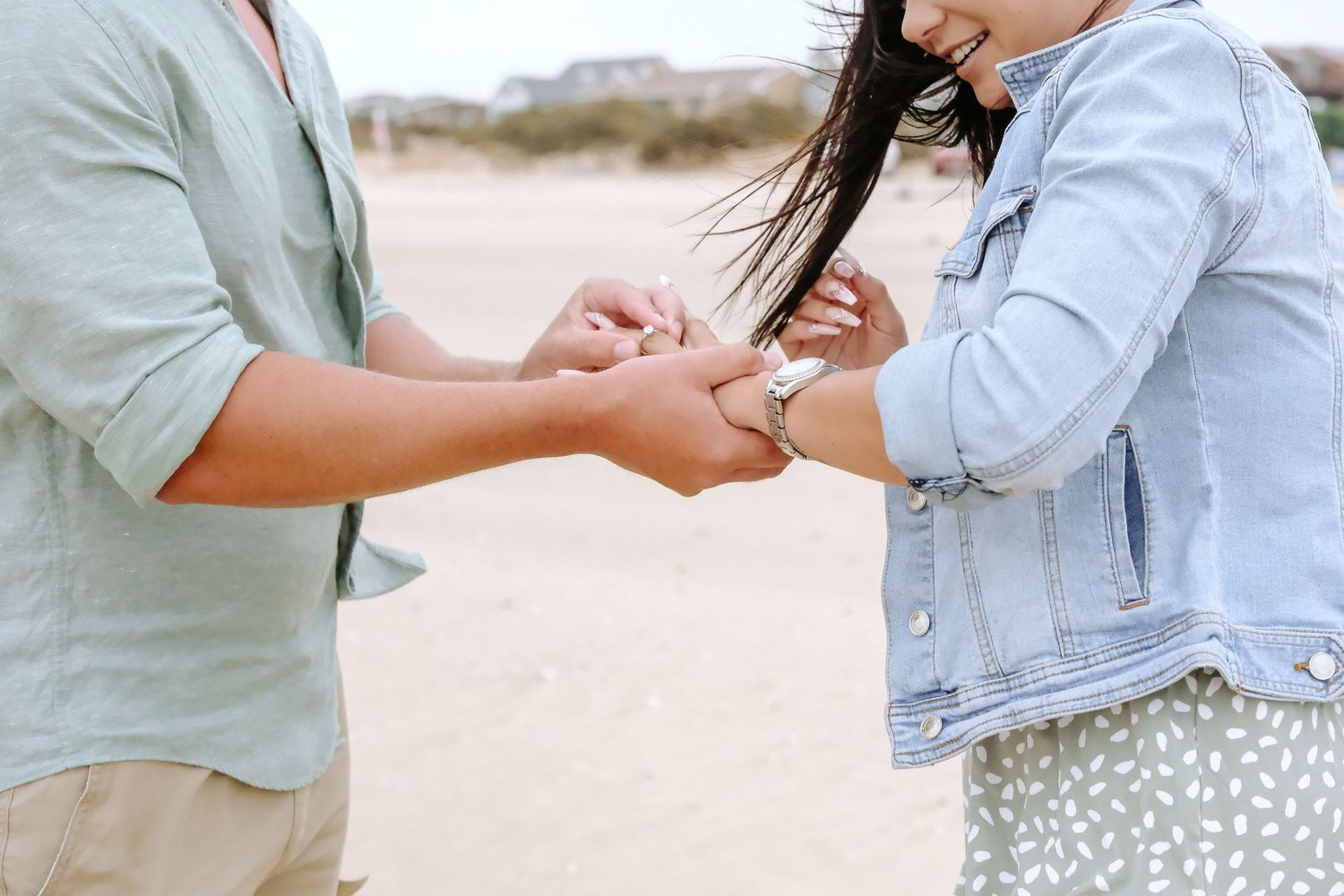 A close up of hands exchanging a ring during a beach proposal.
