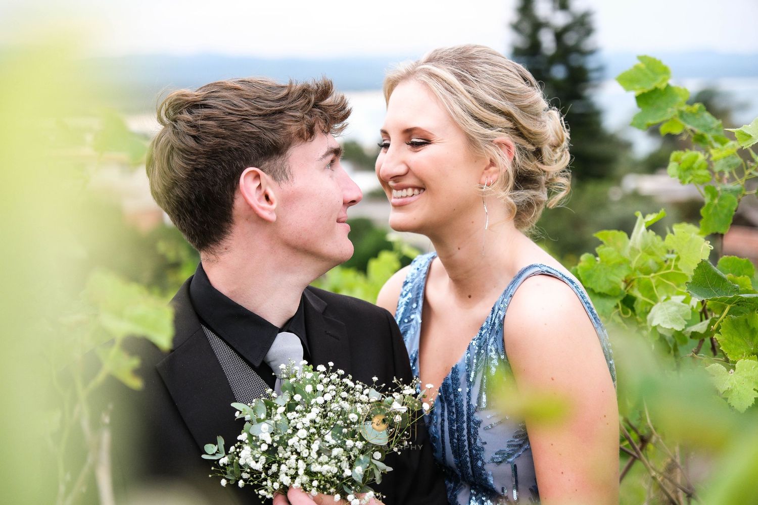 A romantic couple shares an intimate moment among vineyard leaves with white flowers.