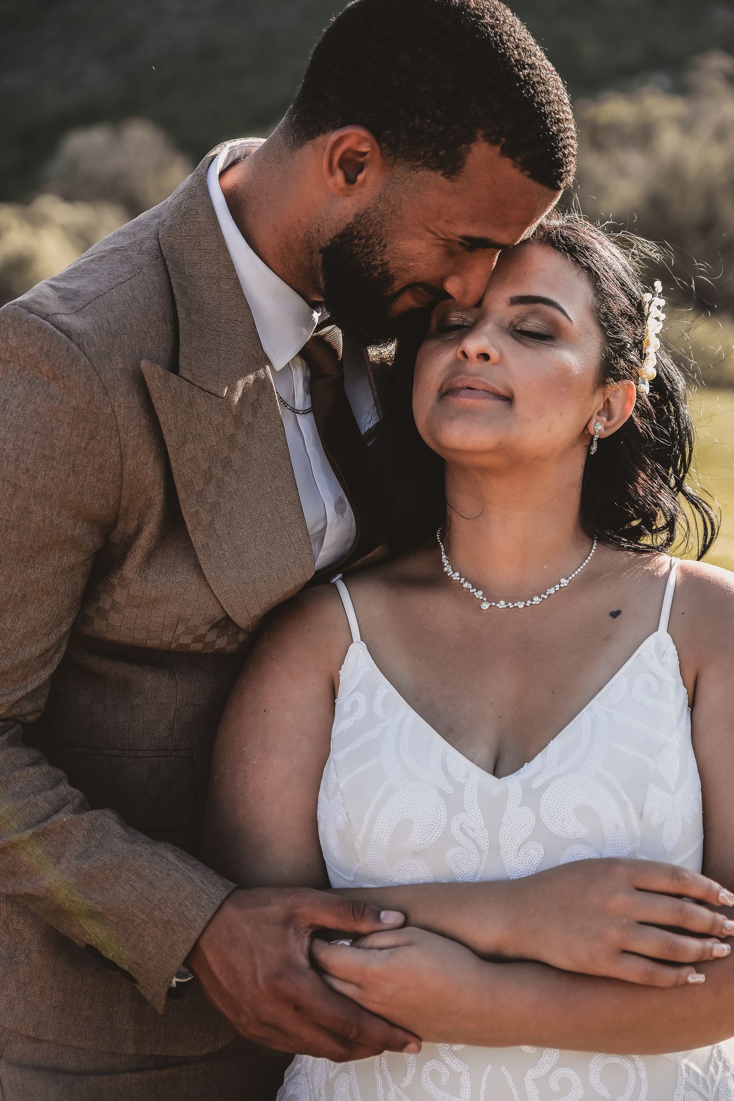 A romantic wedding portrait featuring a couple in a brown suit and white dress at sunset.