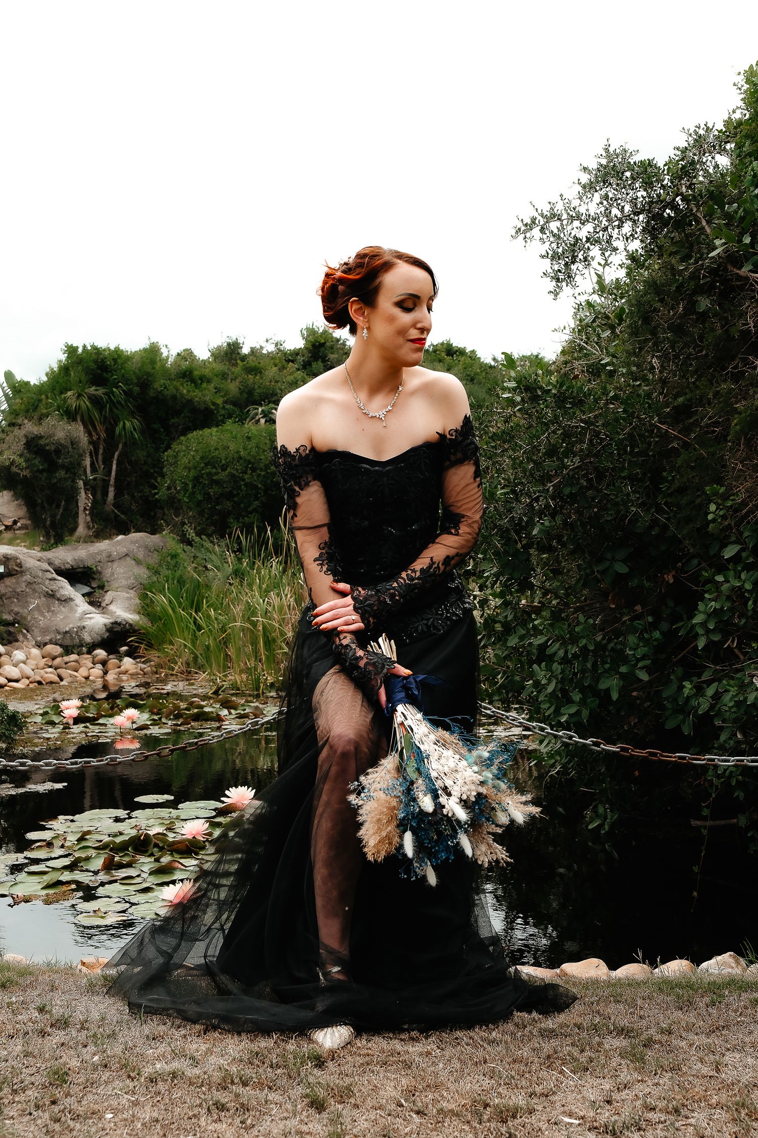 A black formal gown photographed near a pond with natural landscaping.