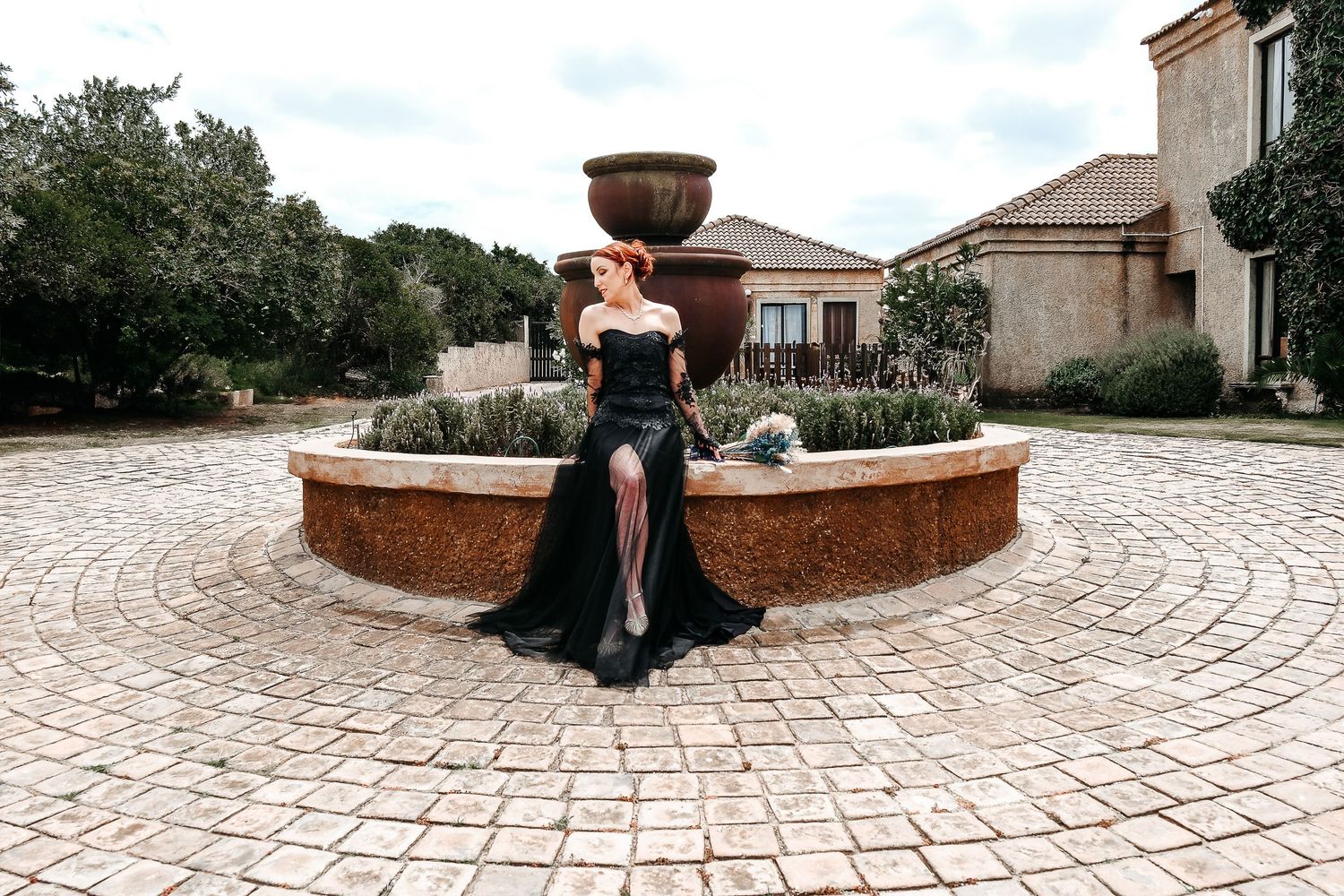 A formal black dress photographed at a circular stone fountain courtyard.