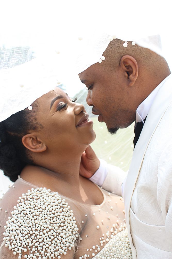 Wedding couple in white formal attire sharing an intimate close-up moment.