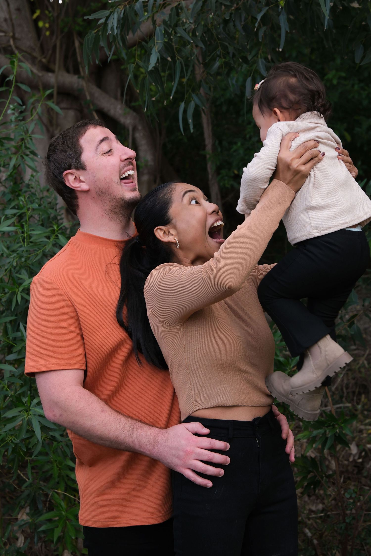 A family playing and laughing together against a leafy backdrop.