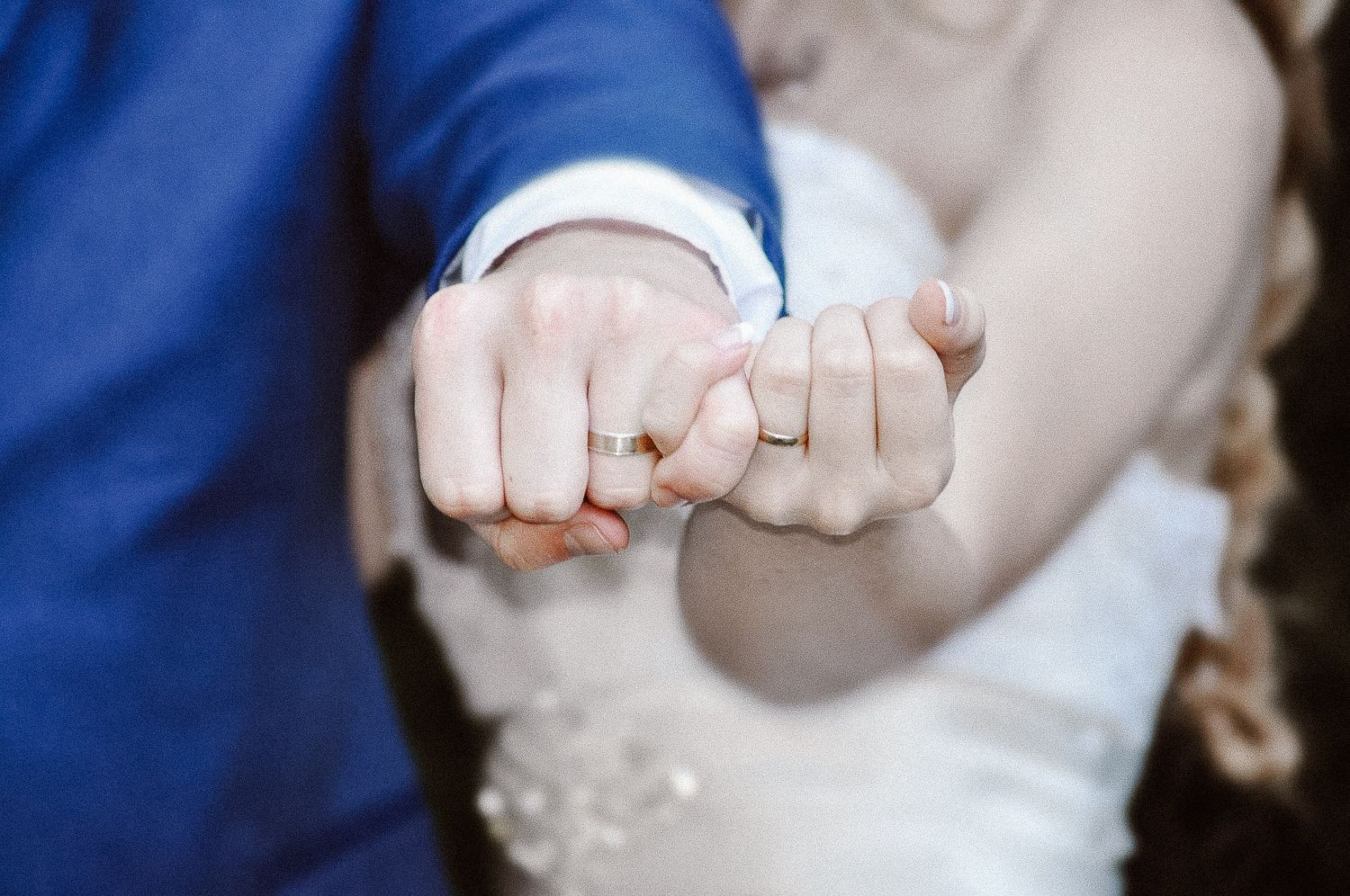 Close-up of newlyweds holding hands showing wedding rings and formal attire details.