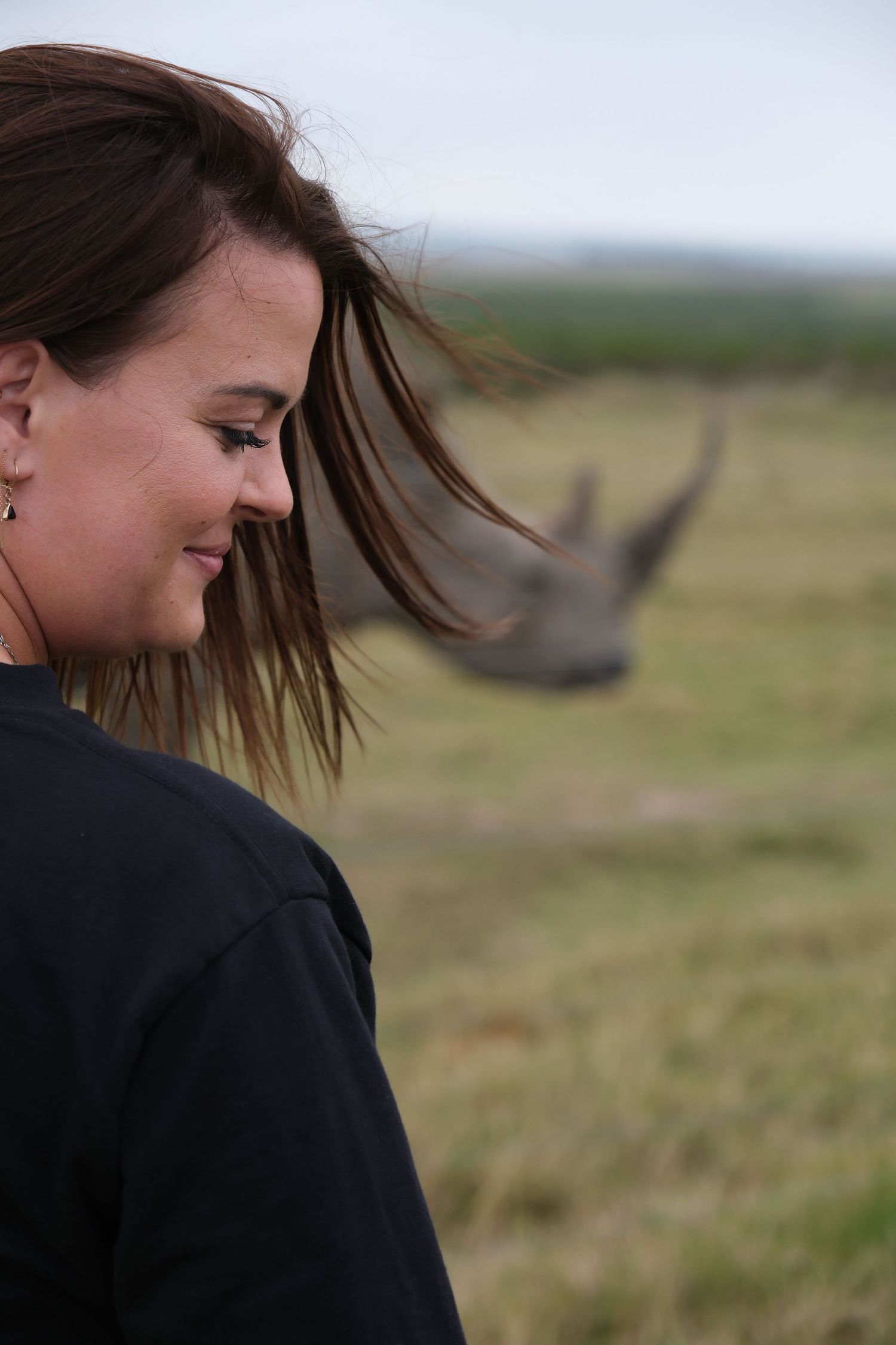 A close-up view of a rhinoceros in the background with windswept hair in the foreground.