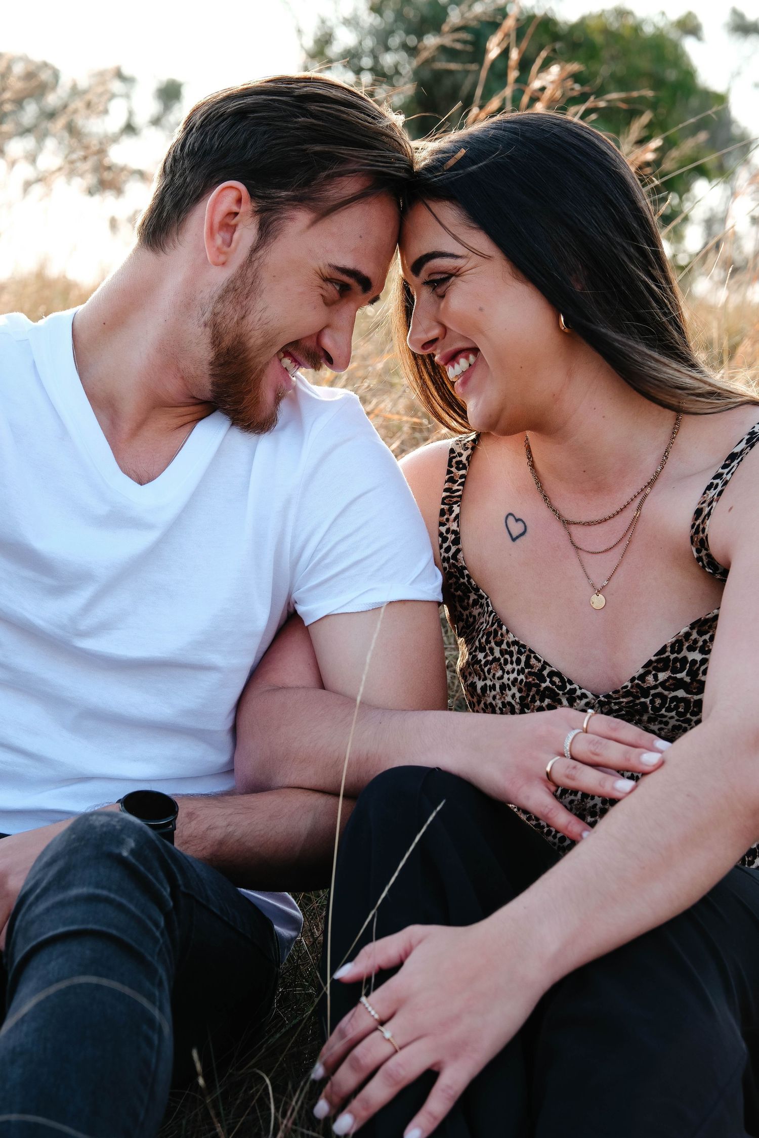 Couple sharing joyful intimate moment while sitting in nature during golden hour.