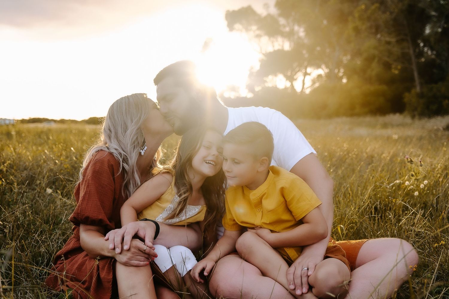 Family enjoying a tender moment together in a golden field at sunset.
