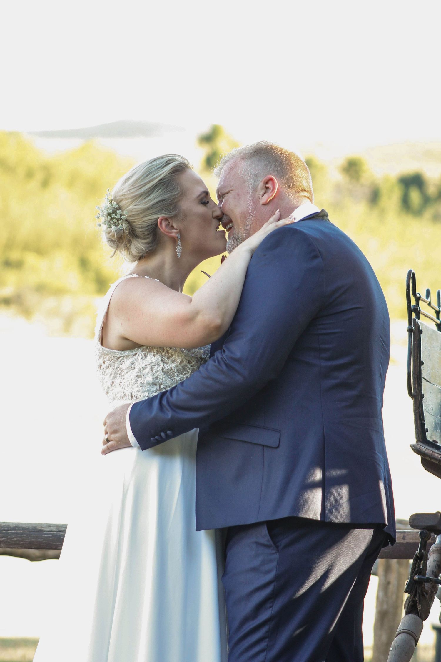 Newlywed couple shares romantic kiss in outdoor wedding ceremony with natural lighting.
