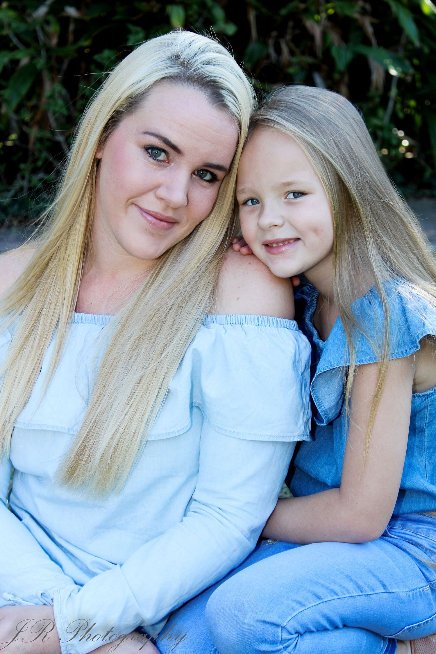 Mother and daughter in matching off-shoulder tops pose together outdoors.