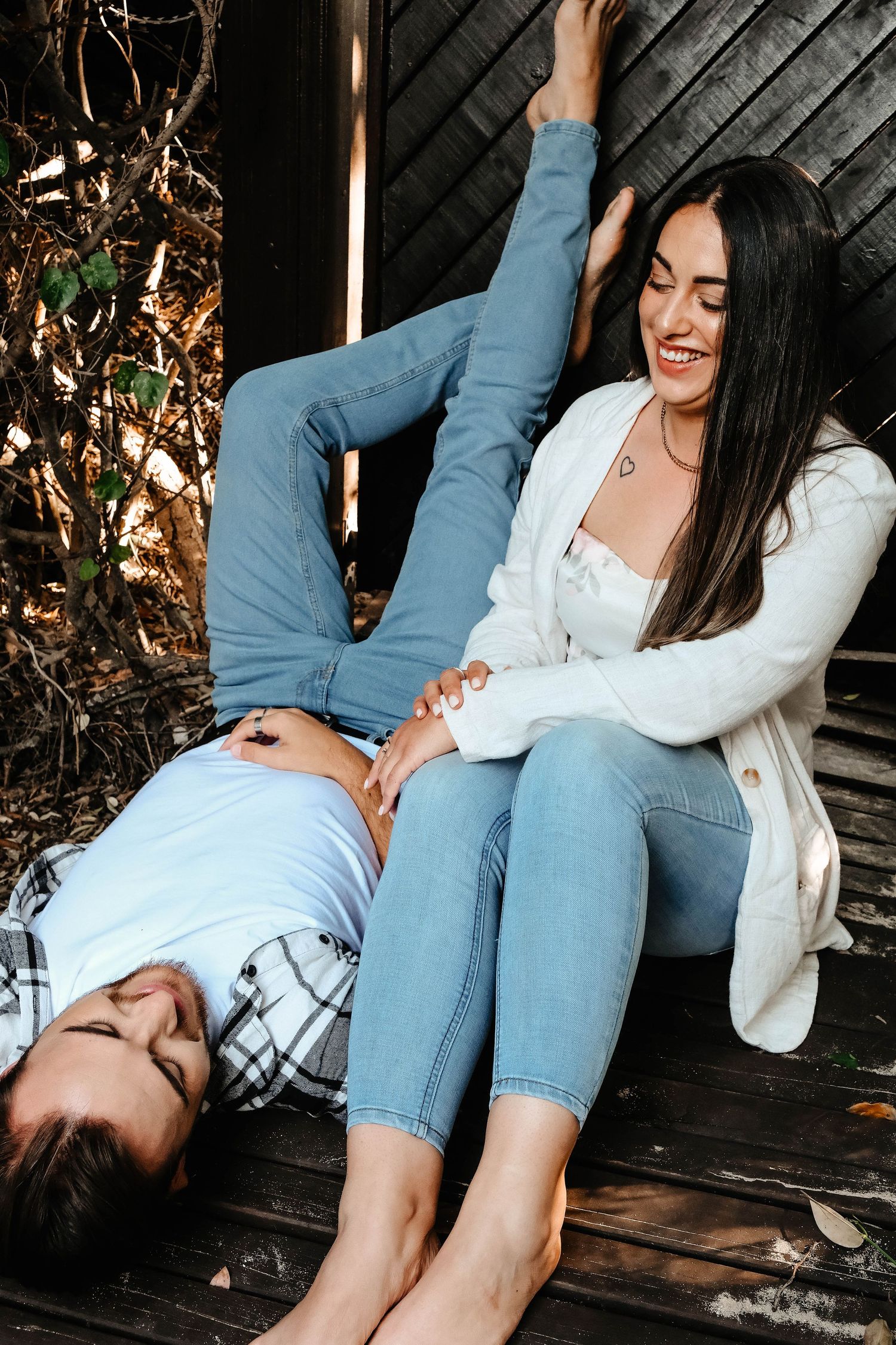 Couple laughing together on wooden deck during casual photo shoot.