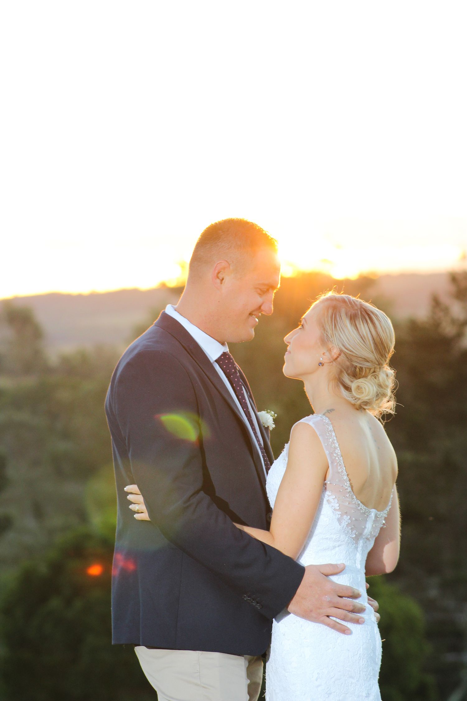 Romantic sunset portrait of newlyweds embracing against a golden sky backdrop.