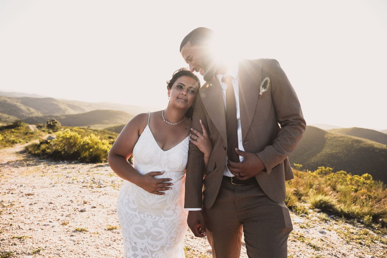 A couple in wedding attire sharing an intimate moment on a sunlit hilltop.