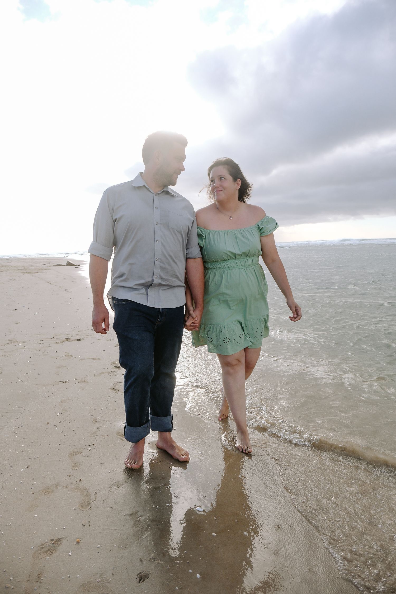 A couple walks hand in hand along a beach shoreline on an overcast day.