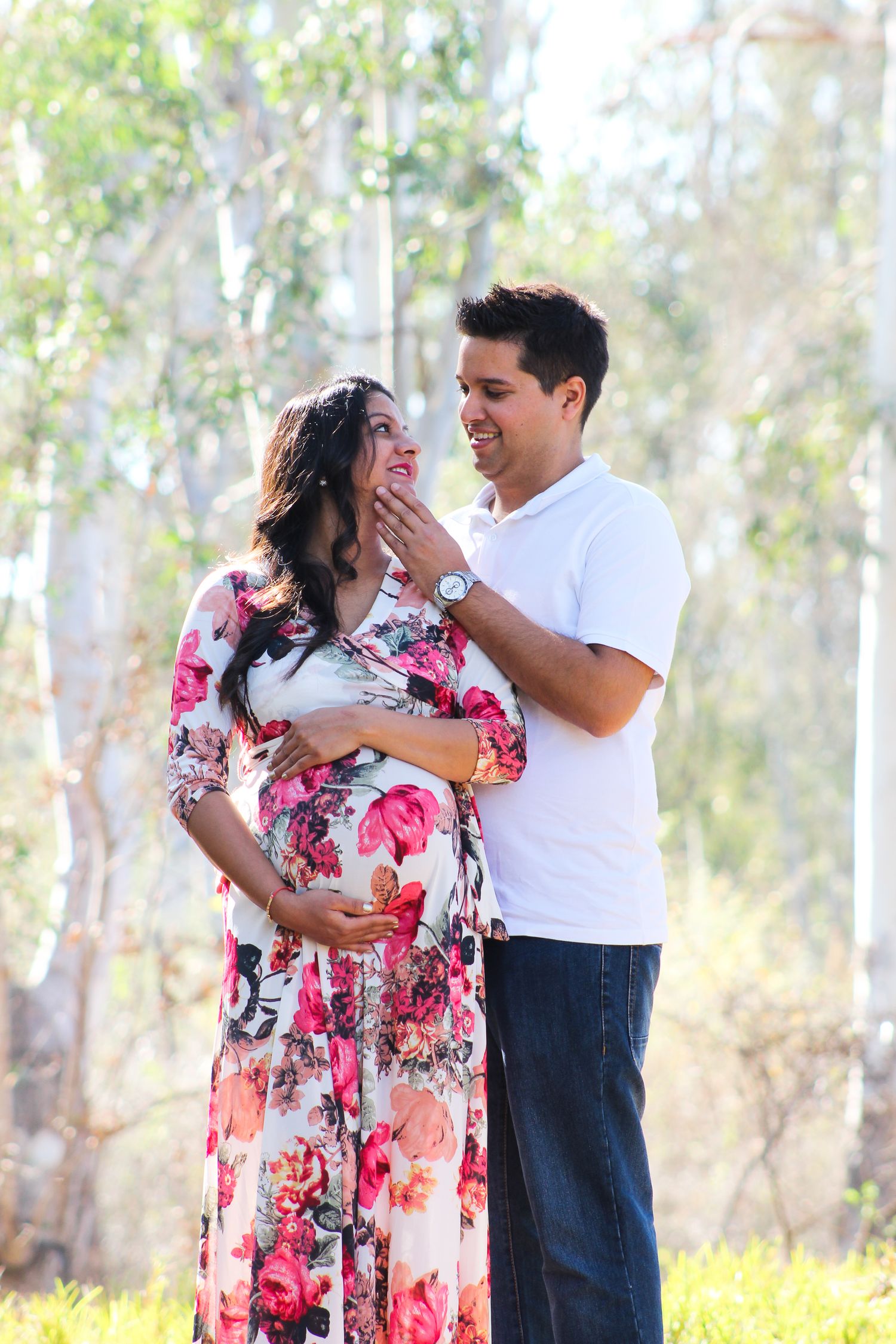 Maternity photo of a couple in a floral dress and white shirt among eucalyptus trees.