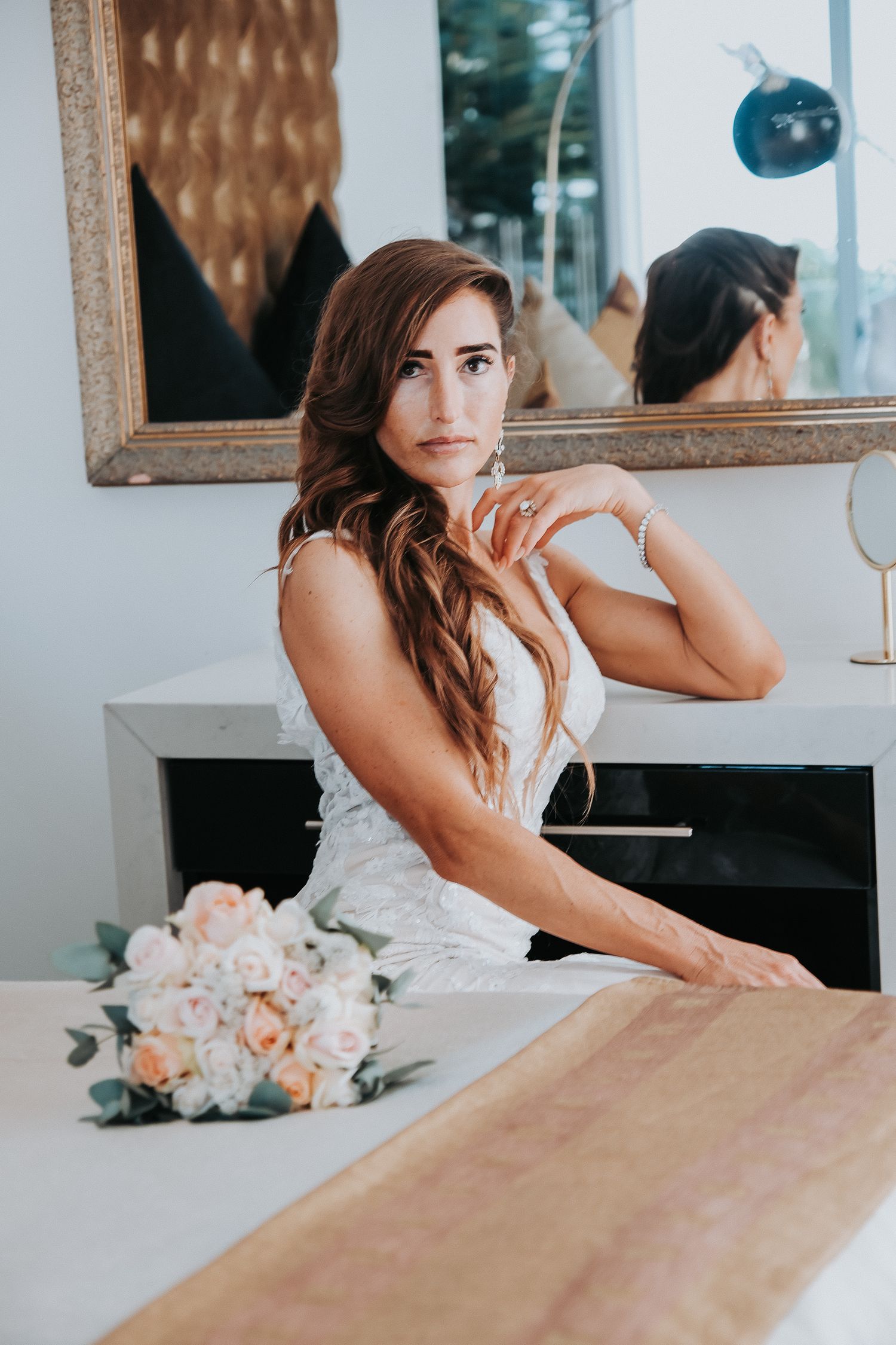 Elegant bridal portrait with floral bouquet and mirror reflection in white room.