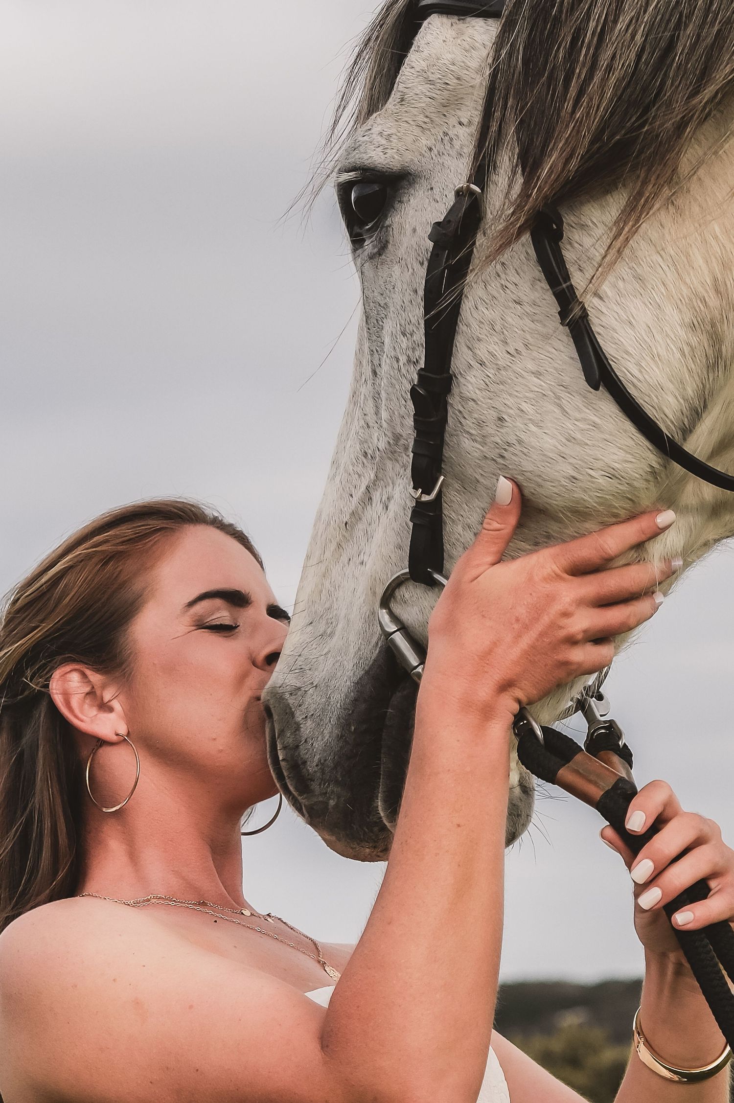 Someone in summer attire shares an intimate moment with a white horse outdoors.