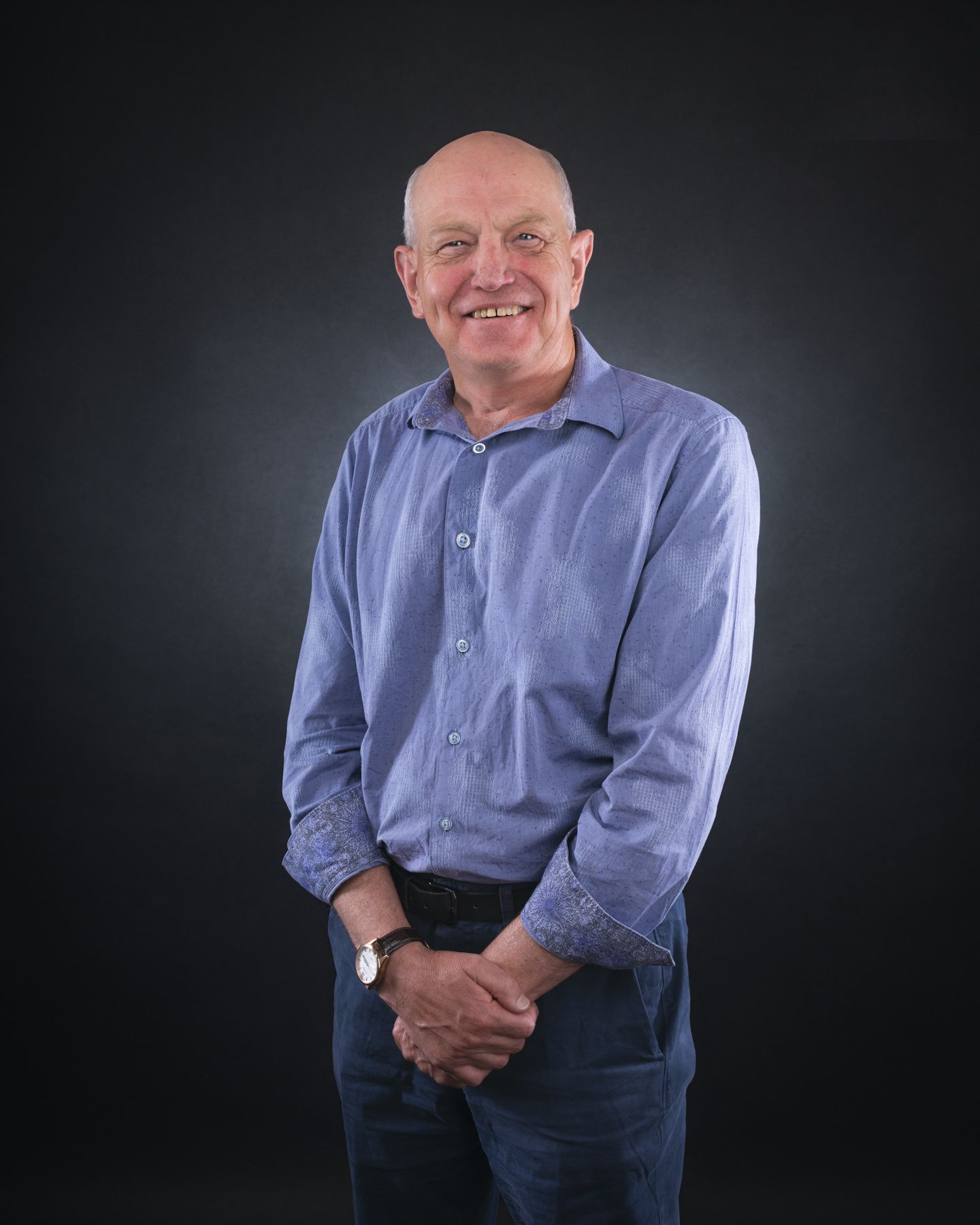Professional studio portrait of someone wearing a light blue button-down shirt against a dark background.