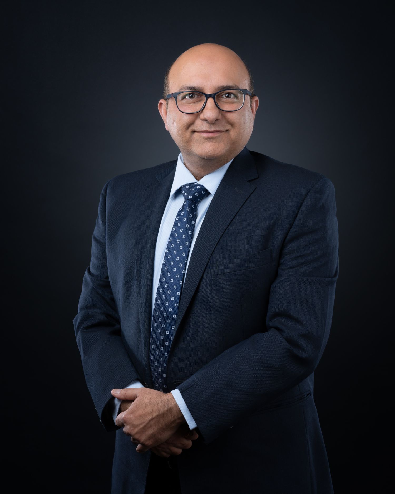 Professional studio portrait of a businessman in a dark suit and polka dot tie against a black background.