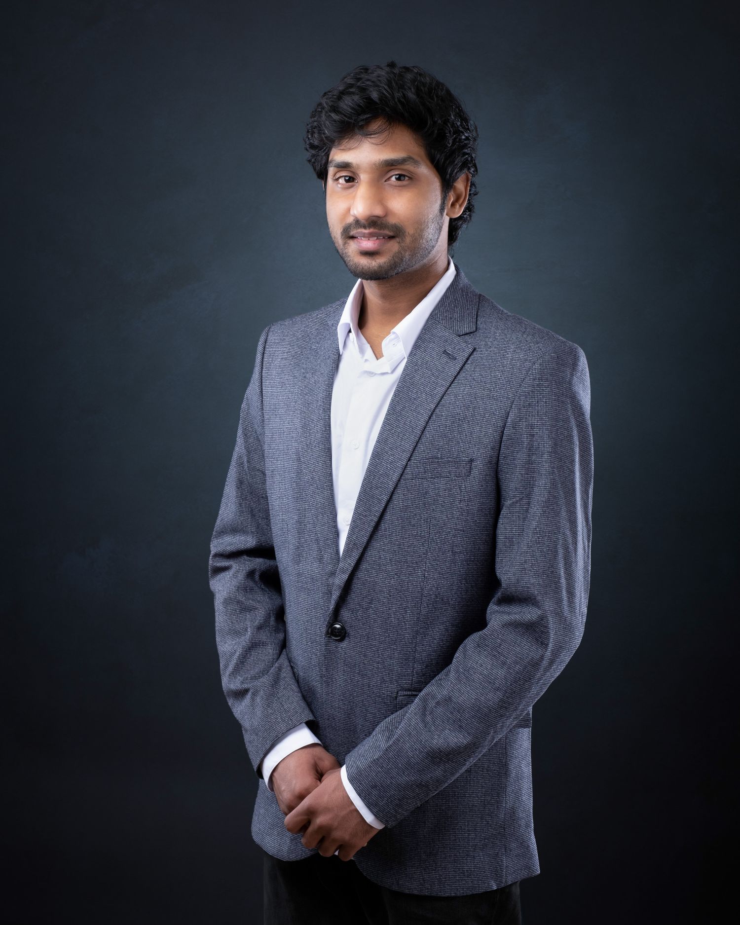 Professional studio portrait of someone wearing a gray suit jacket and white shirt against a dark background.