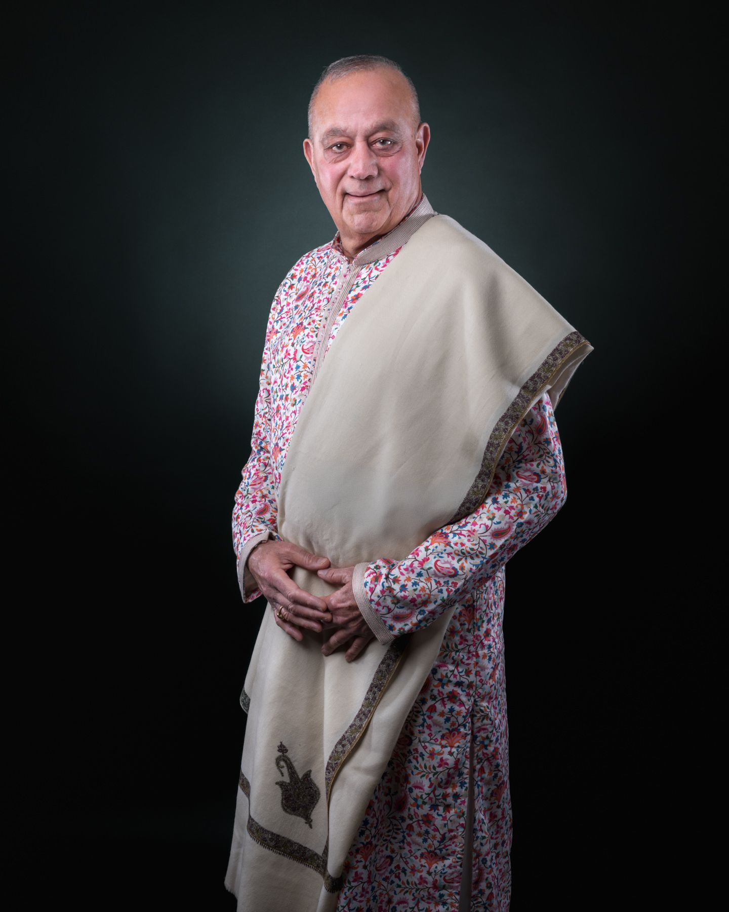 A person wearing a floral print dress and beige shawl poses against a dark background in a series of studio portraits.