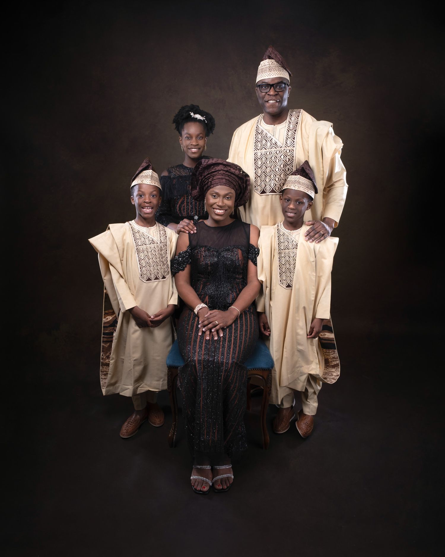 Family portrait featuring traditional African attire including cream-colored agbada robes and modern formal dress against dark backdrop.