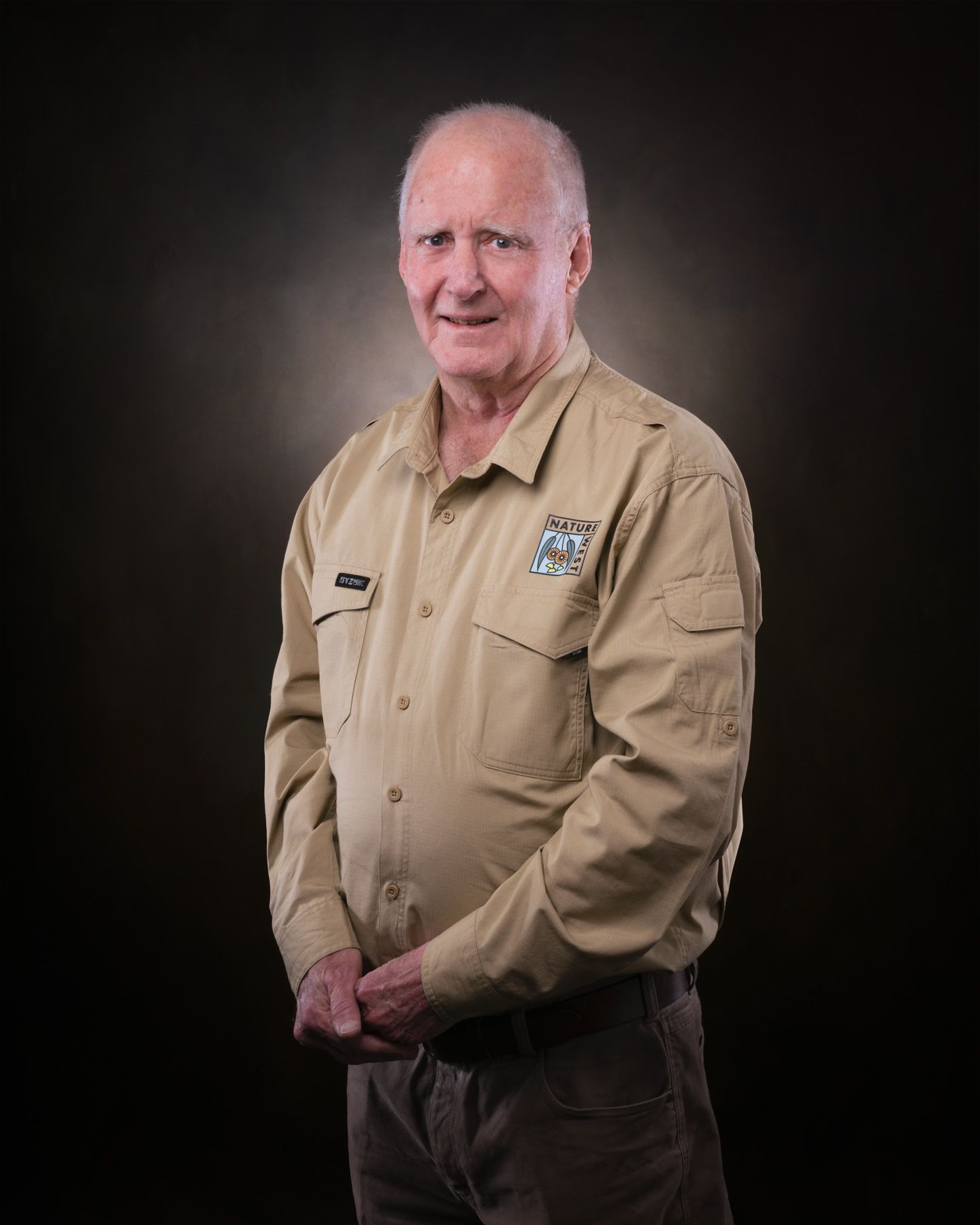 Professional studio portrait of someone wearing a khaki uniform shirt against a dark background.