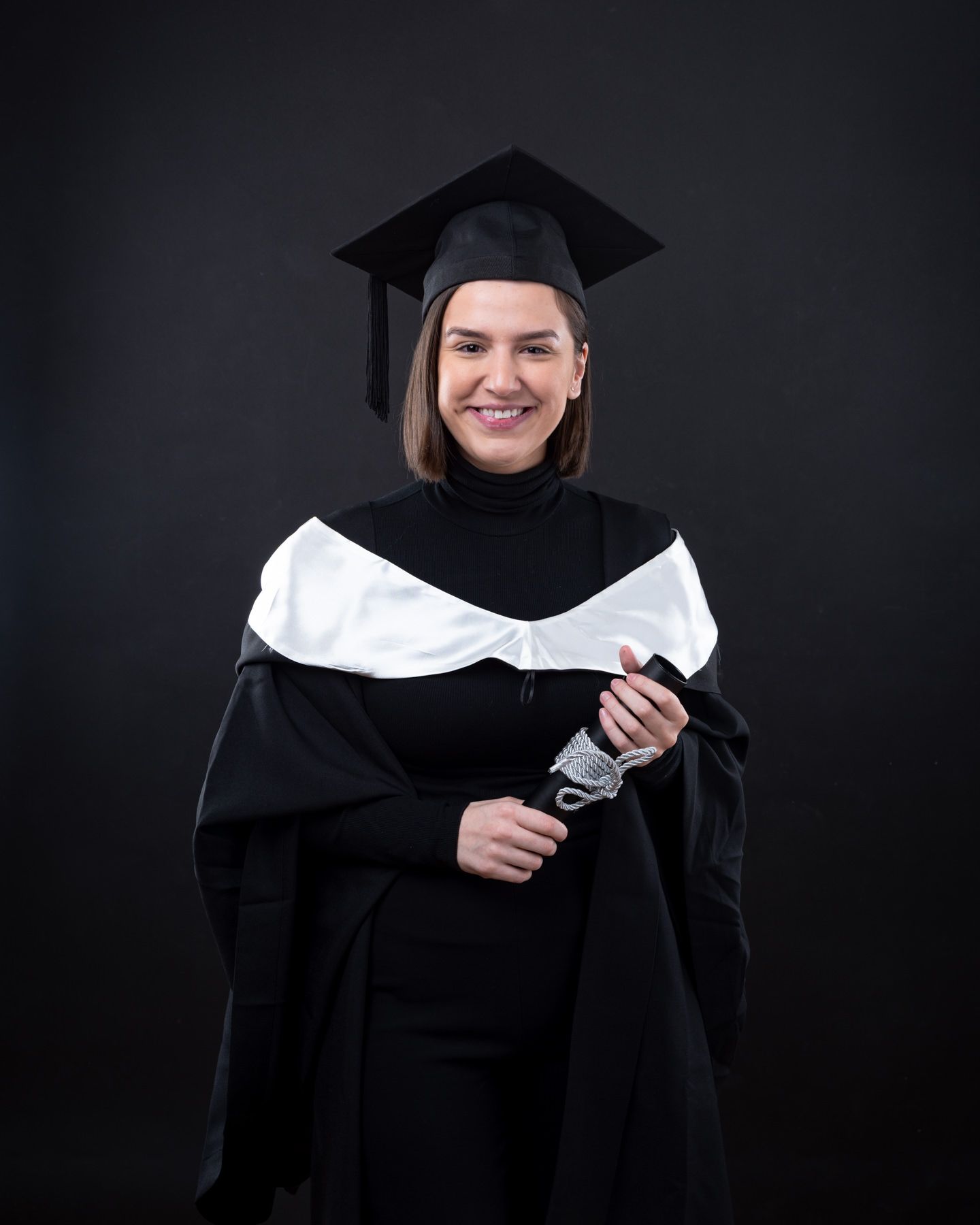 A graduate in black cap and gown holds their diploma against a dark background in a series of celebratory poses.