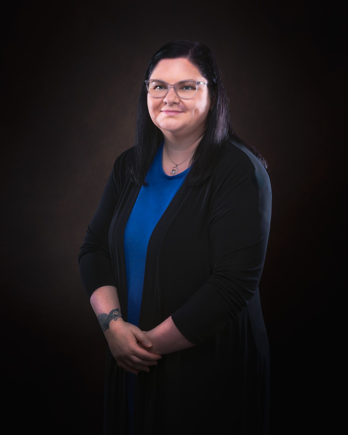 Professional portrait of a person wearing glasses, a blue top and black blazer against a dark background.