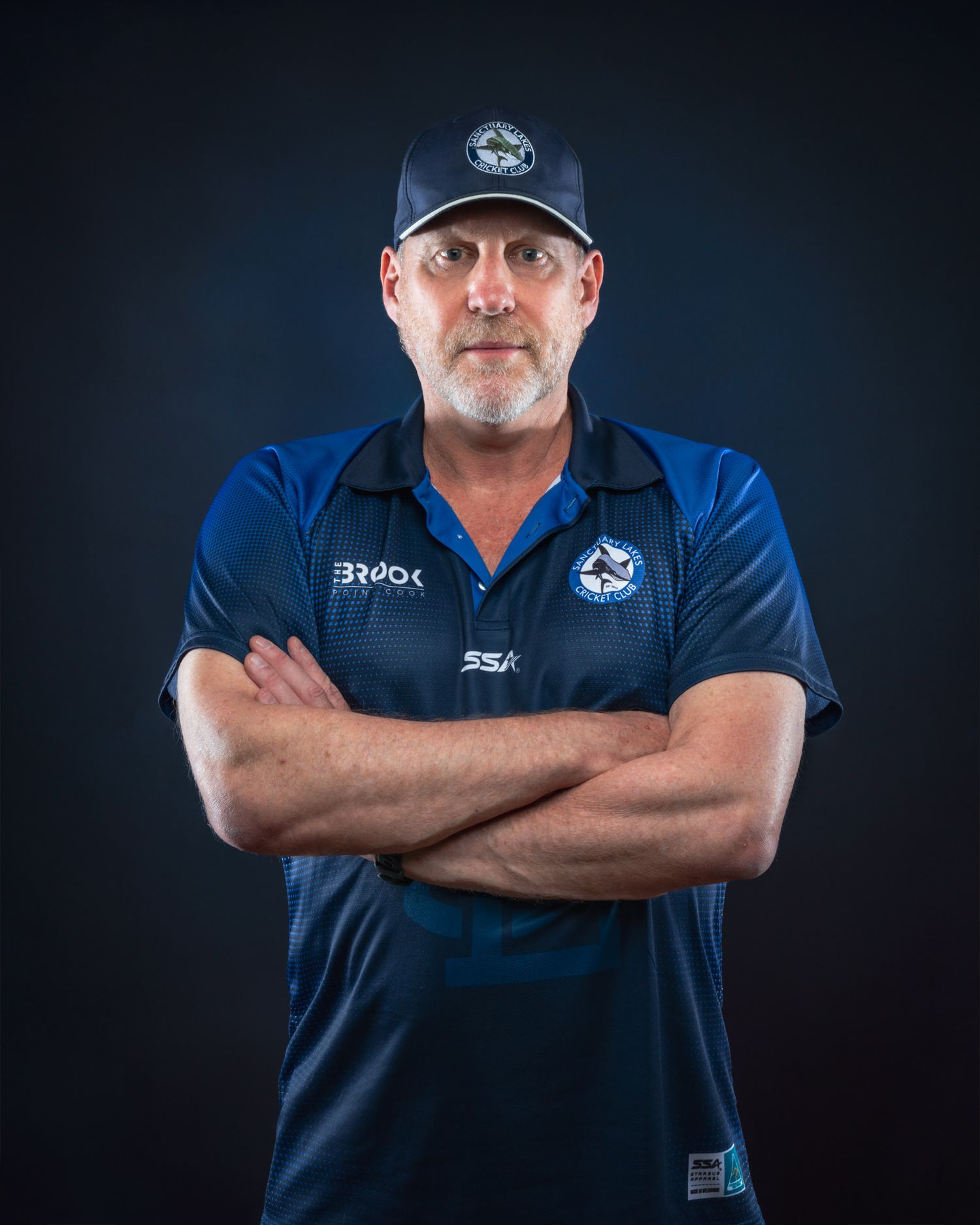 Portrait of someone wearing navy blue team gear with crossed arms while standing against a dark background.