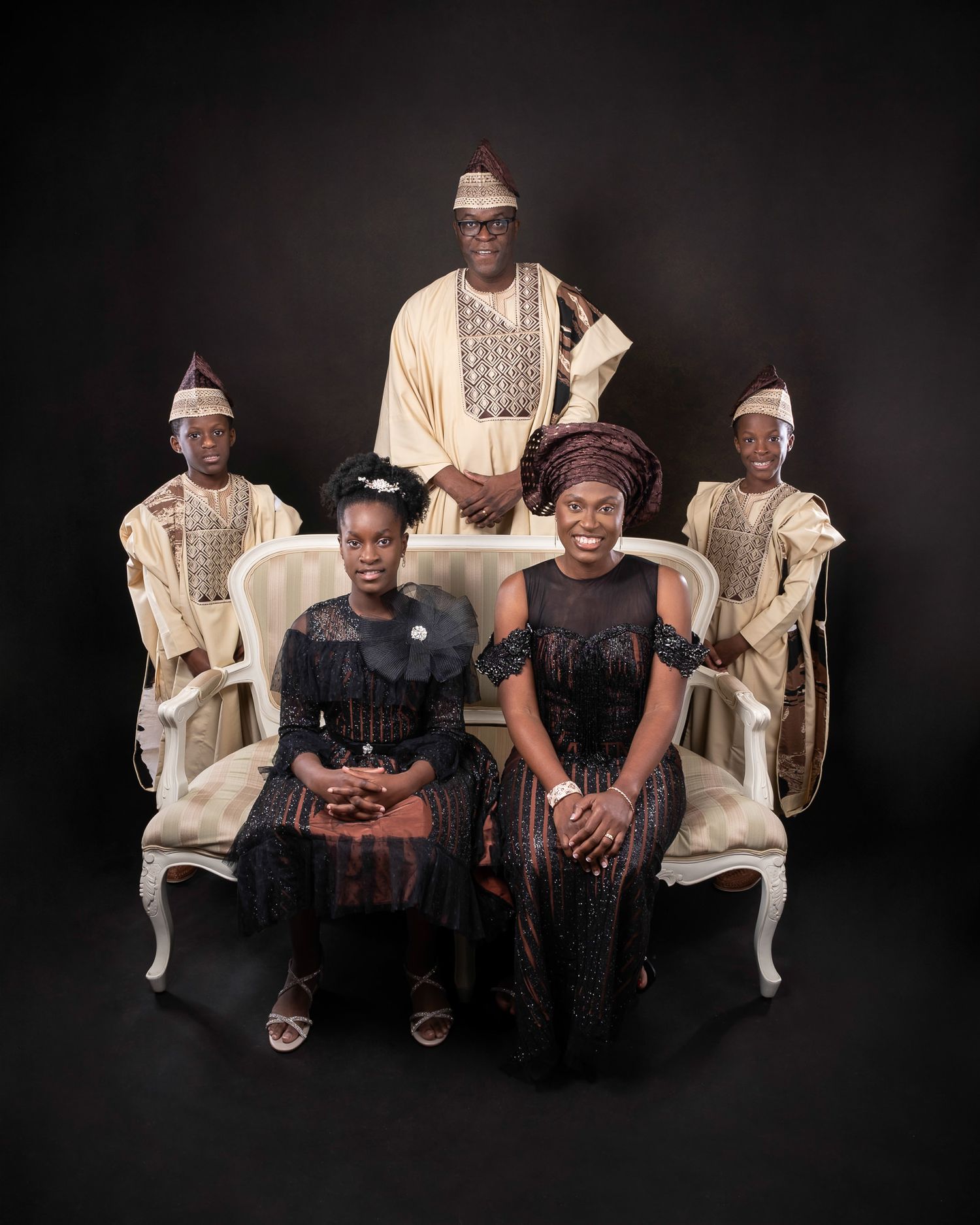 Studio portrait of a family in traditional African attire, with three people wearing white robes and two in black outfits.