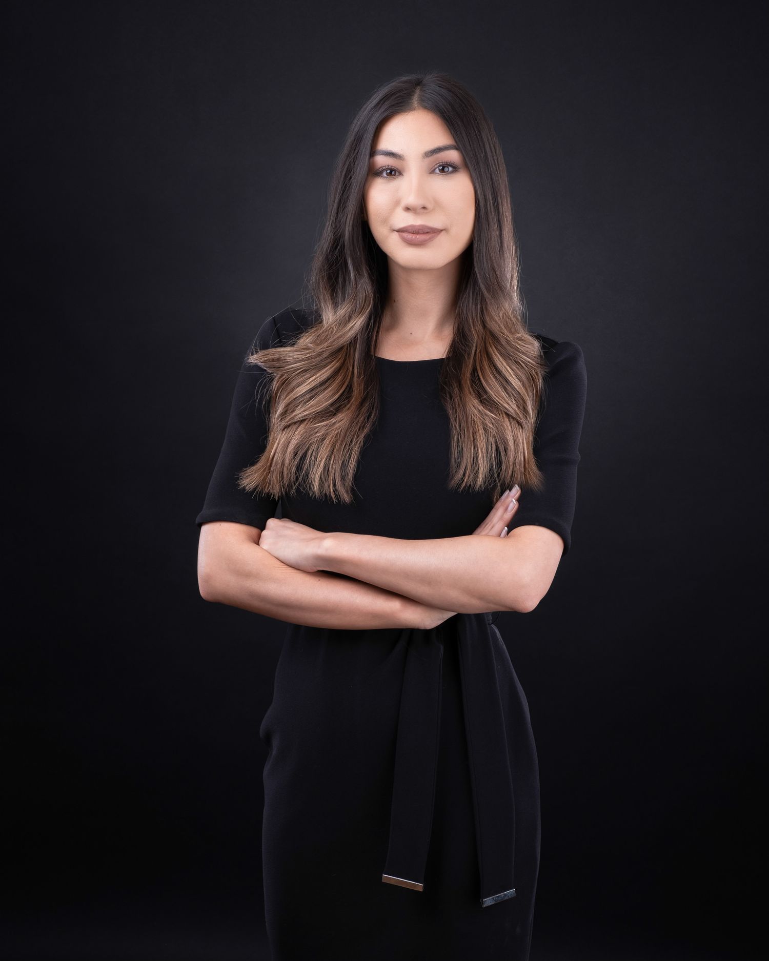 Professional portrait of someone in a black outfit with long brown hair against a dark background.