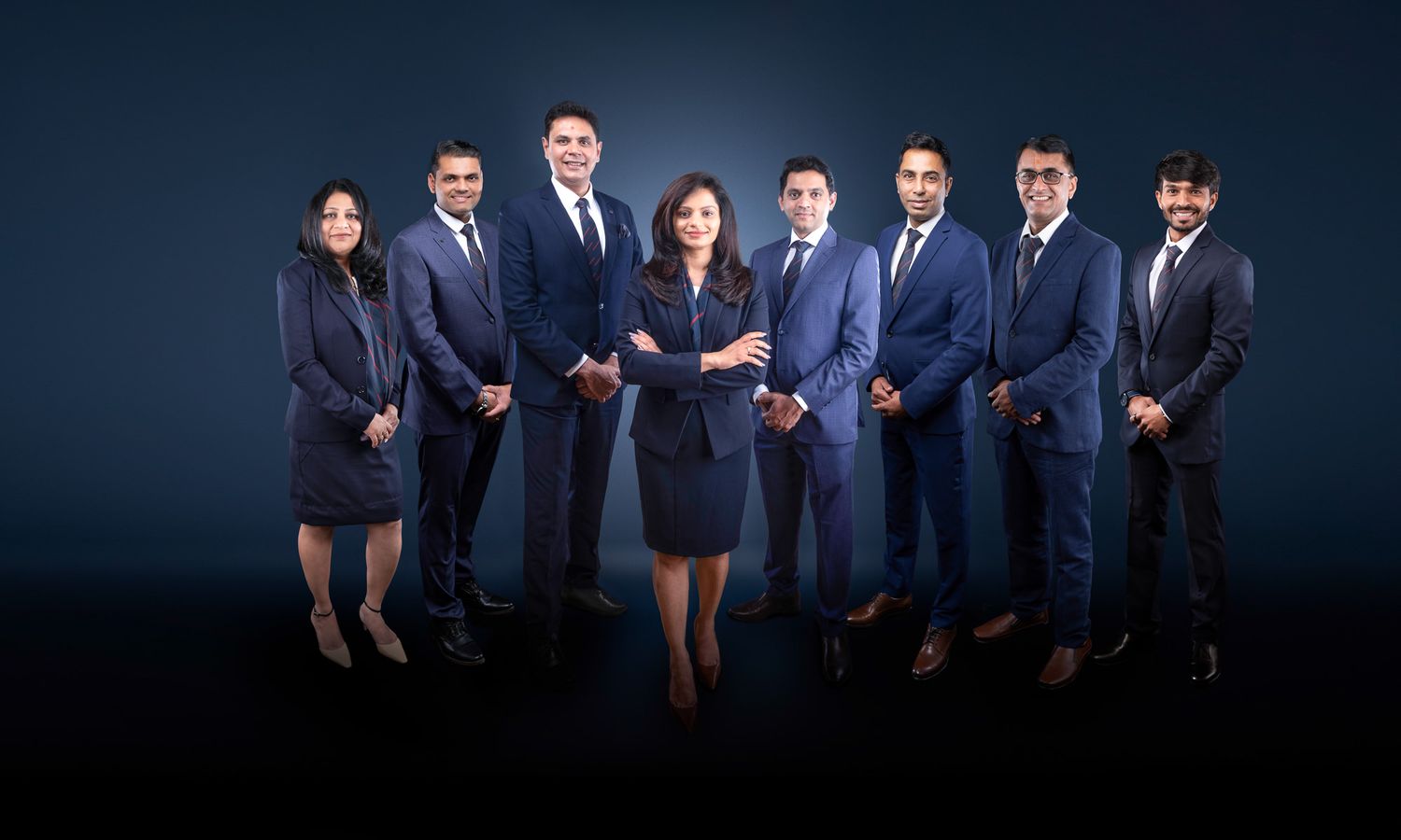 Professional group photo of business team in dark suits against a navy backdrop.