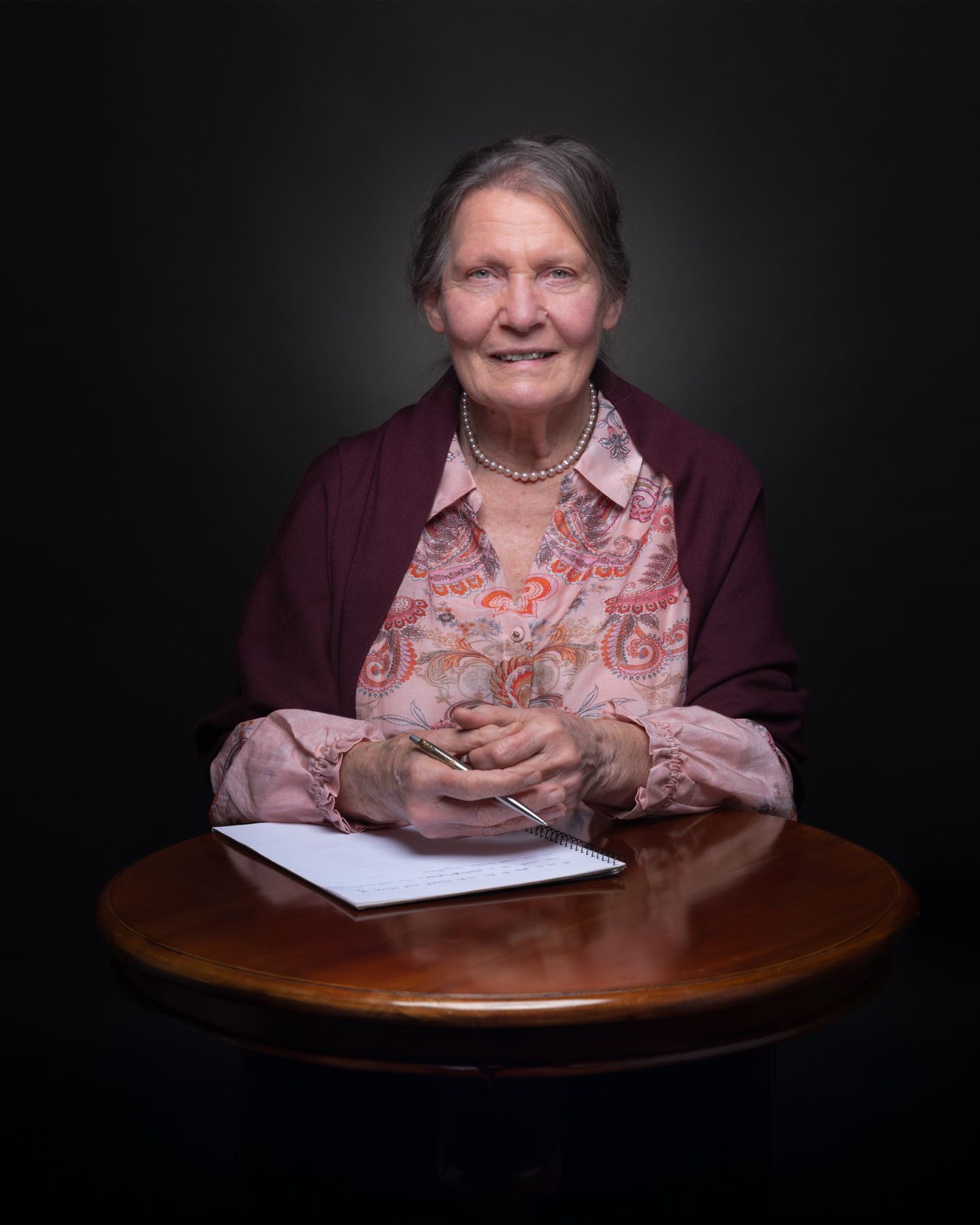 Professional studio portraits showing someone seated at a wooden table against a dark background.