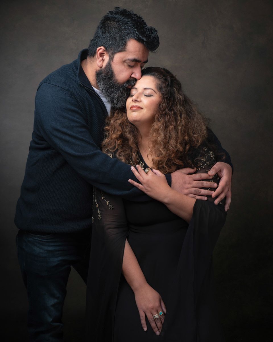 A couple in dark attire share intimate dance-like poses against a dramatic shadowy backdrop in a romantic photo series.