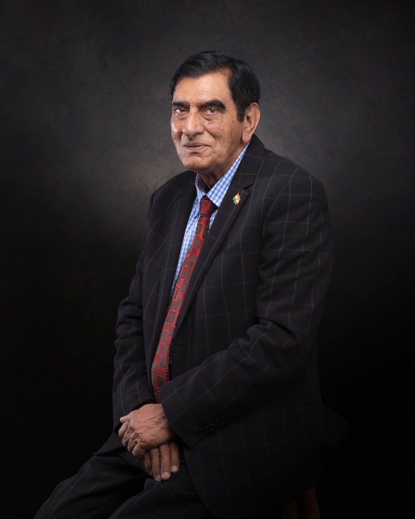 Professional studio portrait of someone in a dark suit and red tie against a black background.