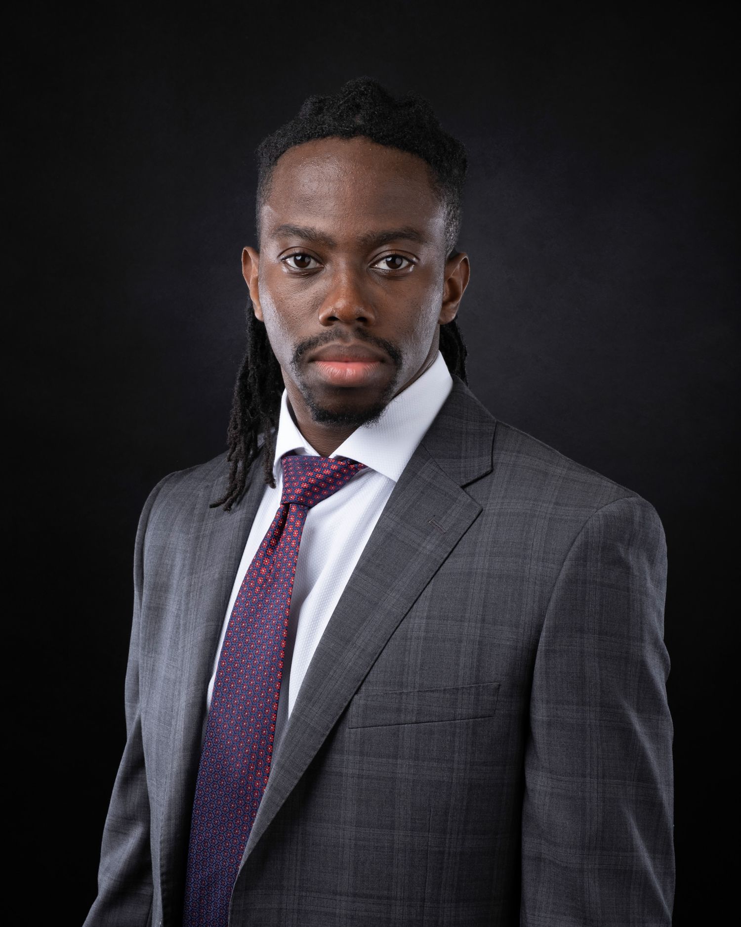 Professional headshot of a person wearing a gray suit and burgundy tie against a dark background.