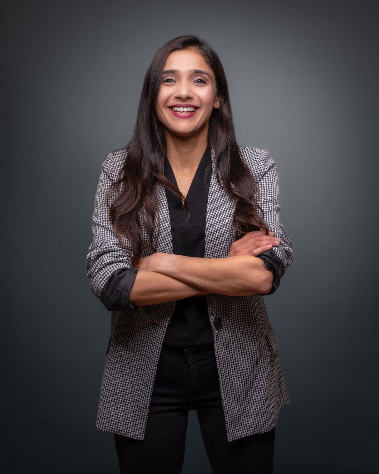Professional wearing a black and white patterned blazer poses with crossed arms against dark background.