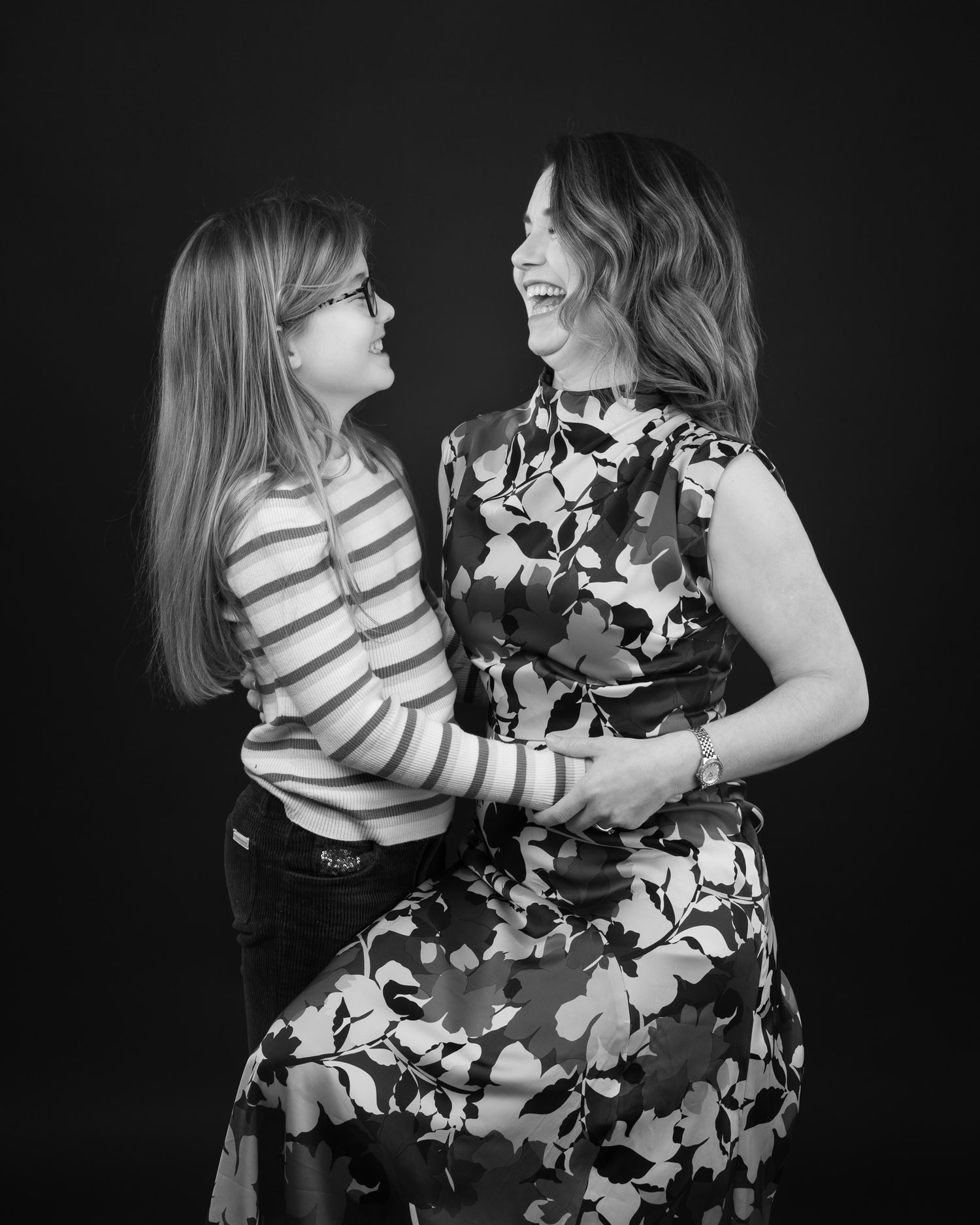 A black and white portrait shows two figures sharing a joyful moment against a dark background.