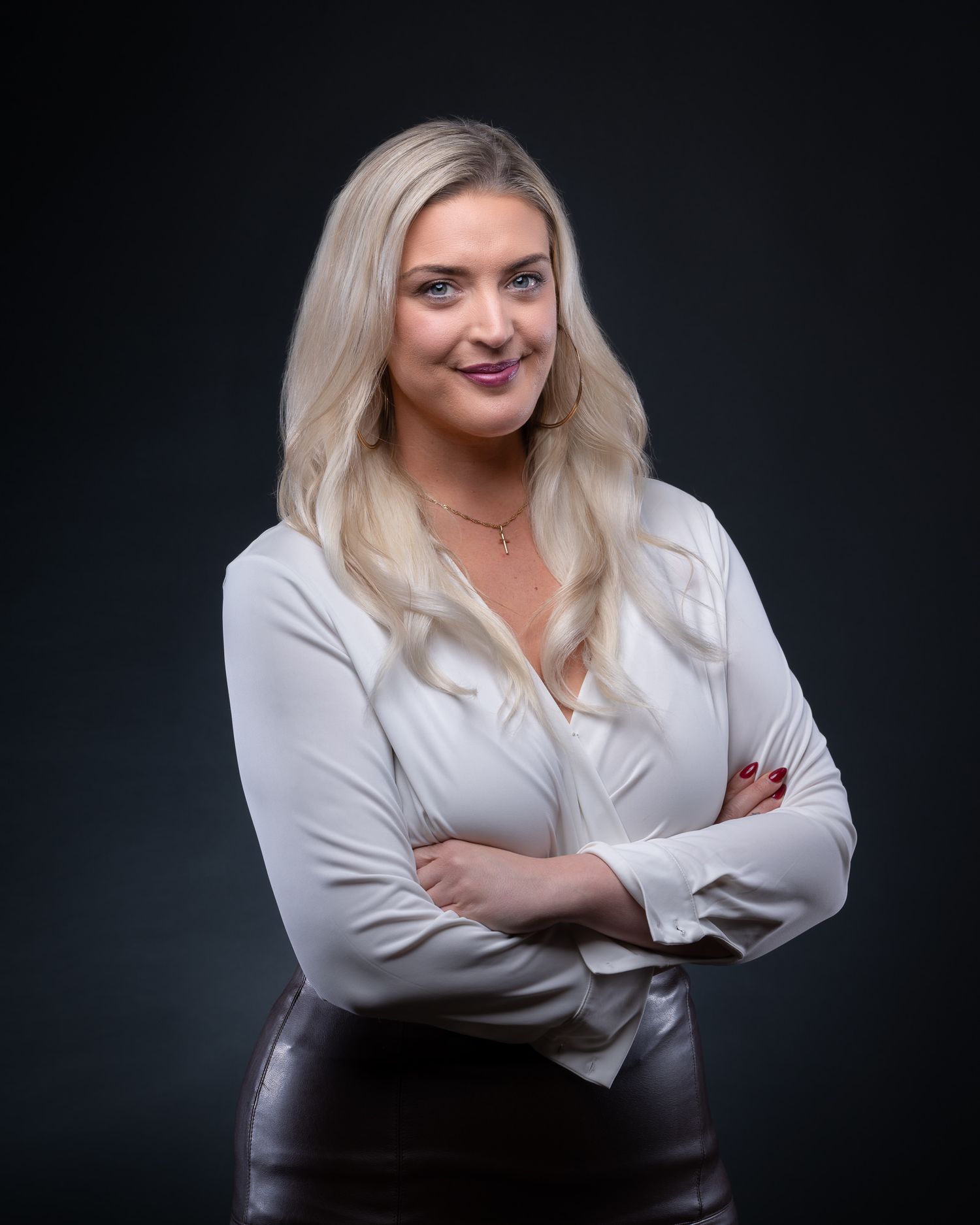 Professional business portrait of a person in a white blouse and dark skirt against a black background.