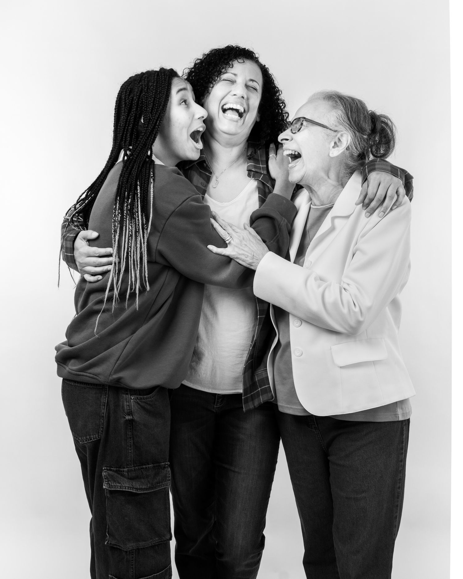 Three friends embrace while laughing joyfully together in a black and white studio portrait photograph.