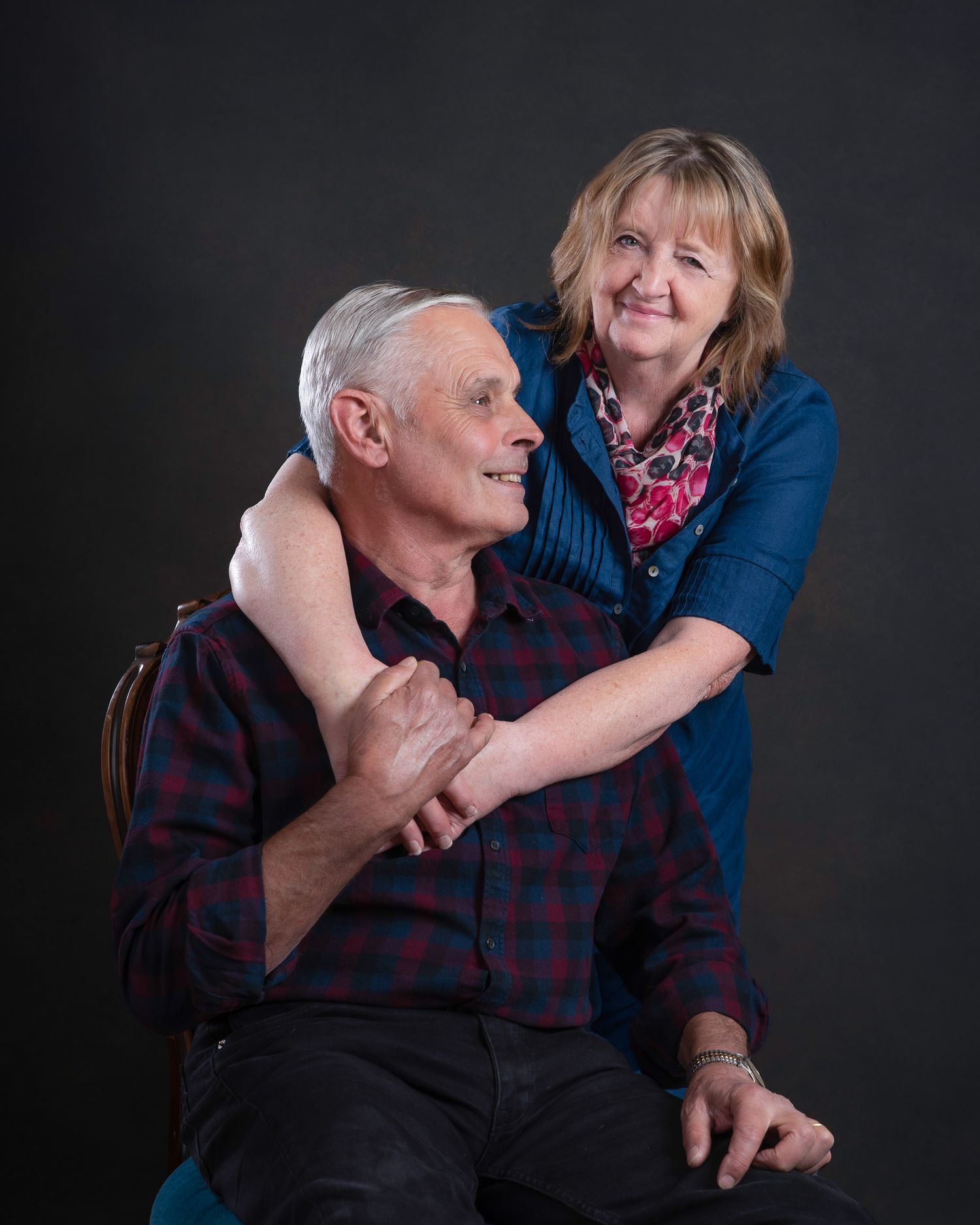 A warm embrace between loved ones wearing blue and plaid against a dark studio backdrop.