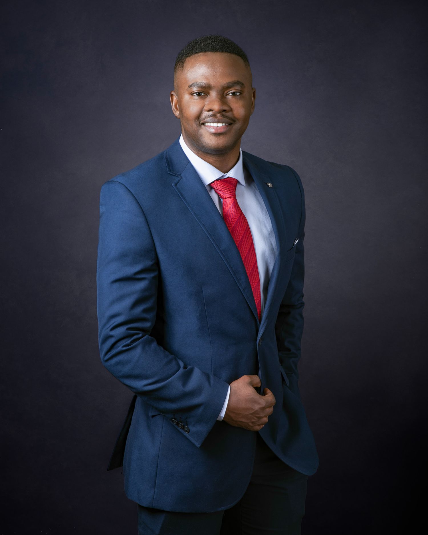 Professional headshot portrait against dark background wearing navy suit and red tie in studio lighting.