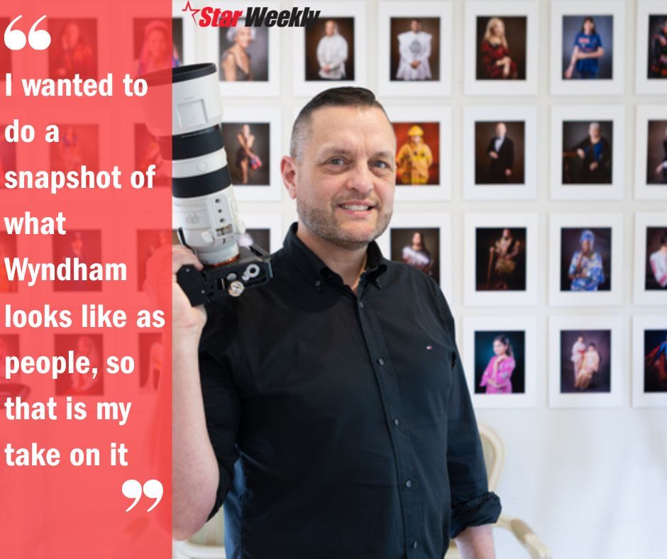 A person in a black jacket stands in front of a wall of small portrait photographs.