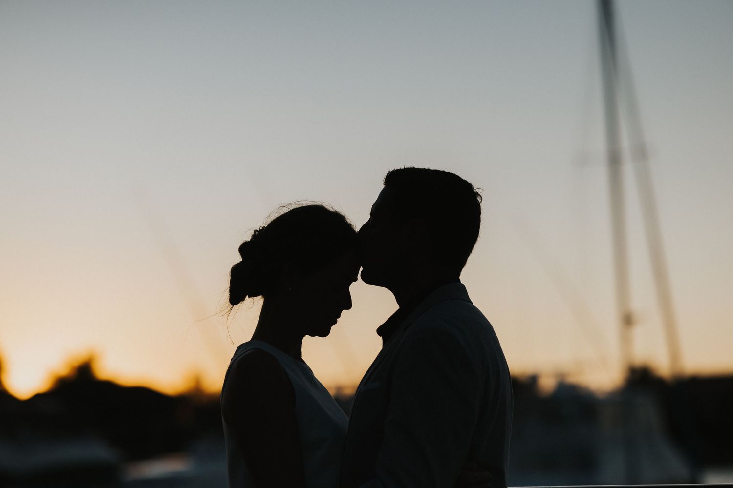 Silhouetted couple sharing romantic moment at sunset against marina backdrop.