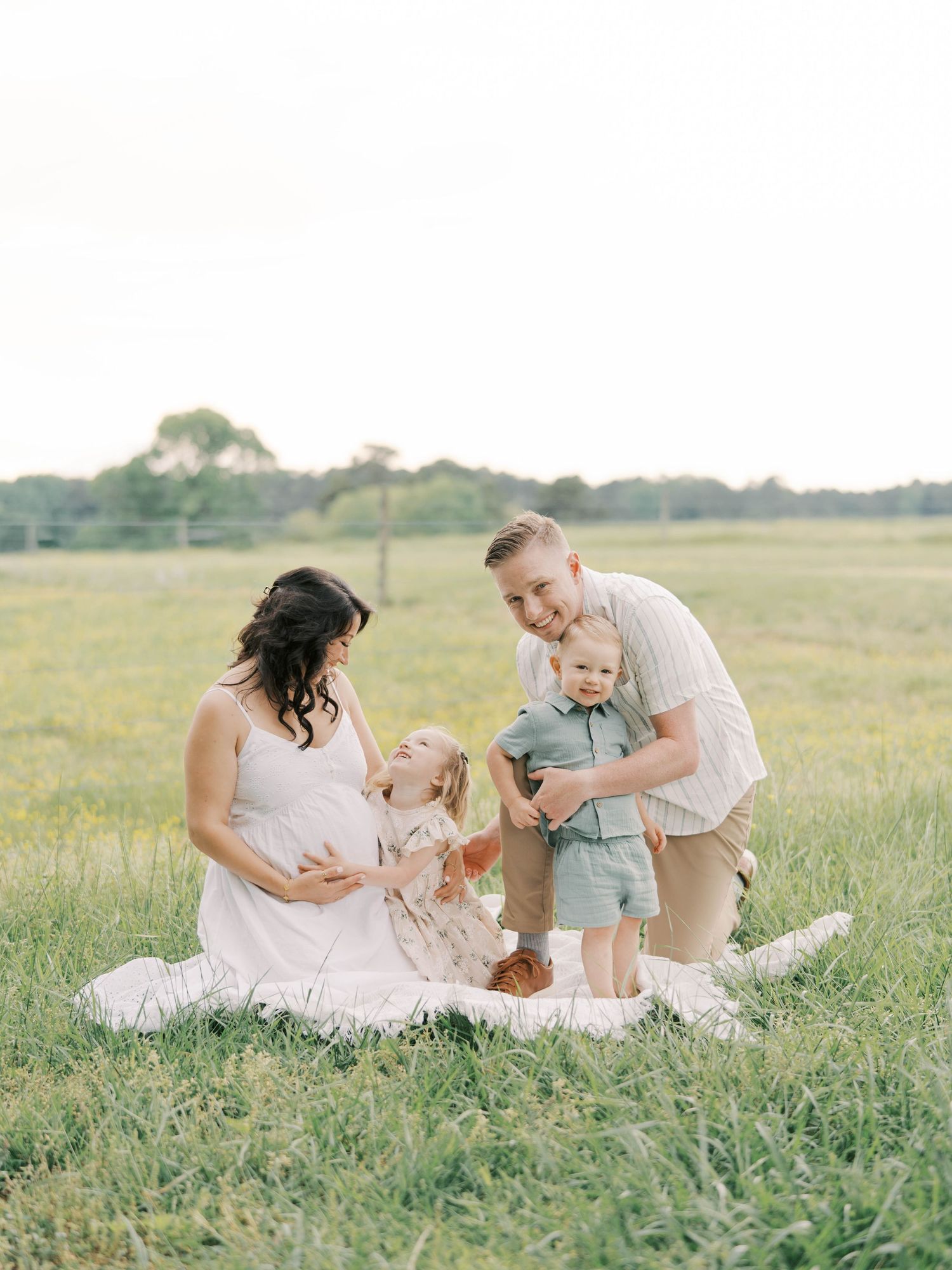 Family gathering on blanket in golden field during sunset photo session.