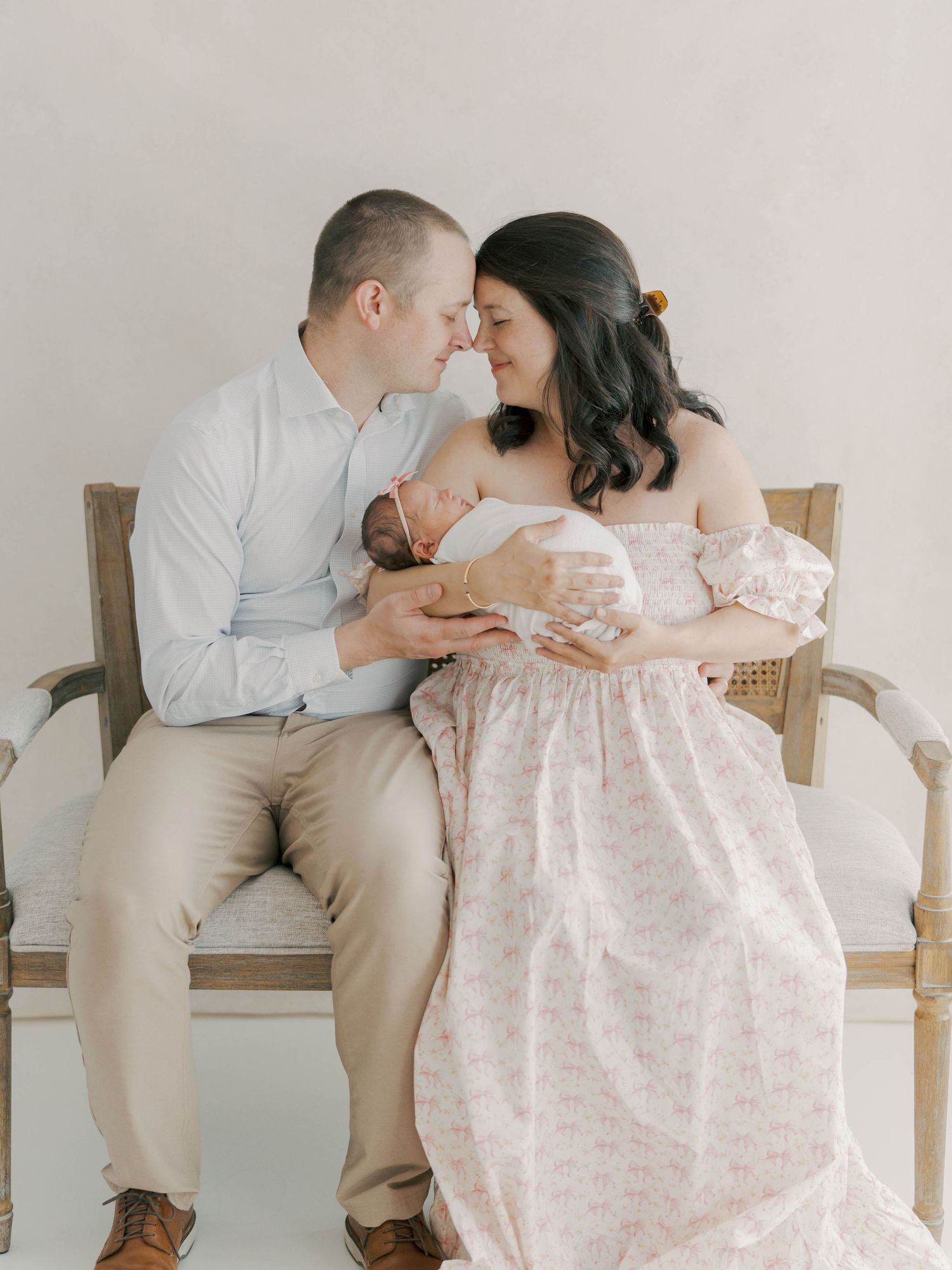 Intimate portrait of couple sharing tender moment with newborn baby on wooden bench.