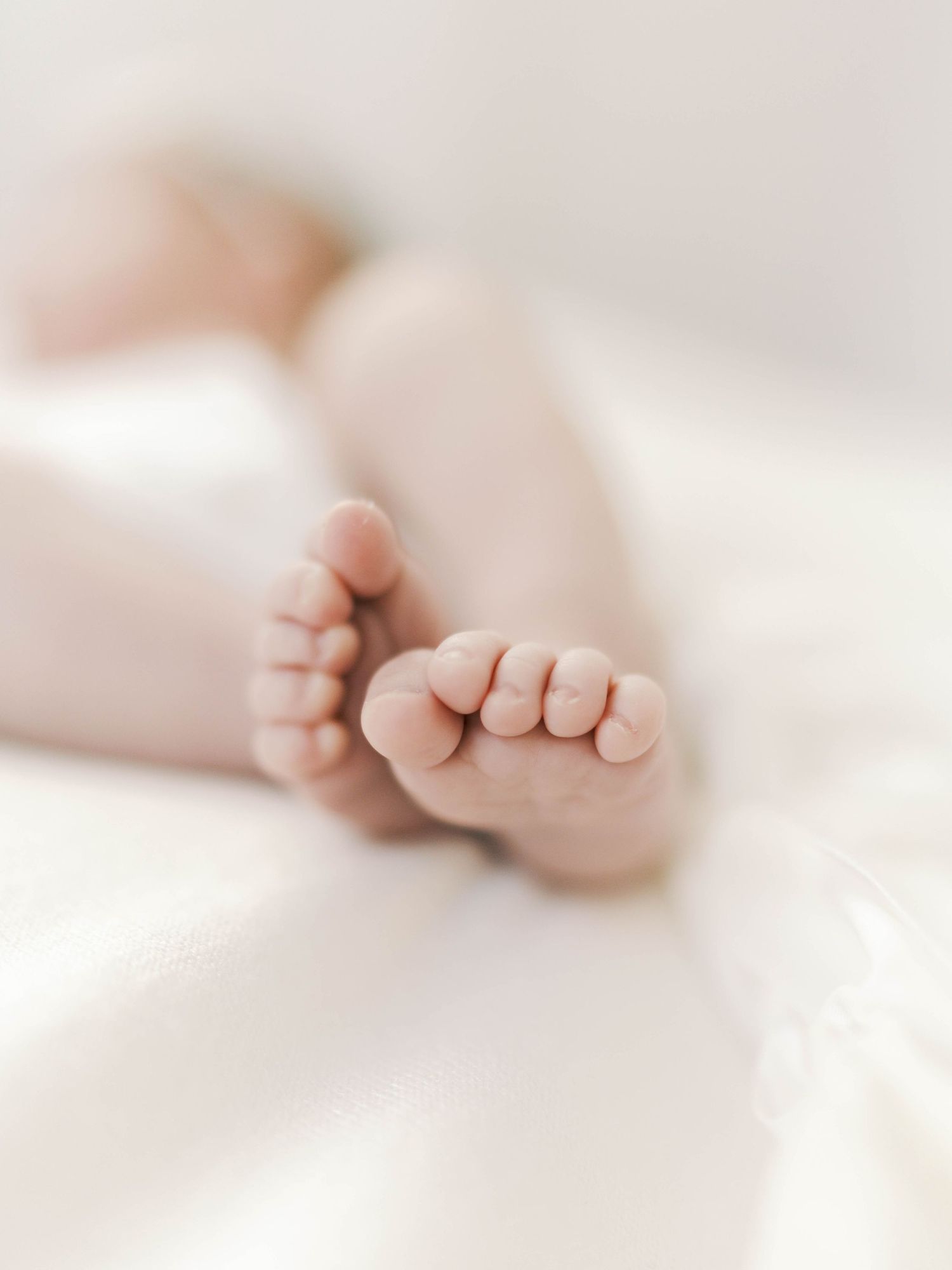 Close-up of tiny newborn baby feet resting on a soft white blanket, perfect for birth announcements.