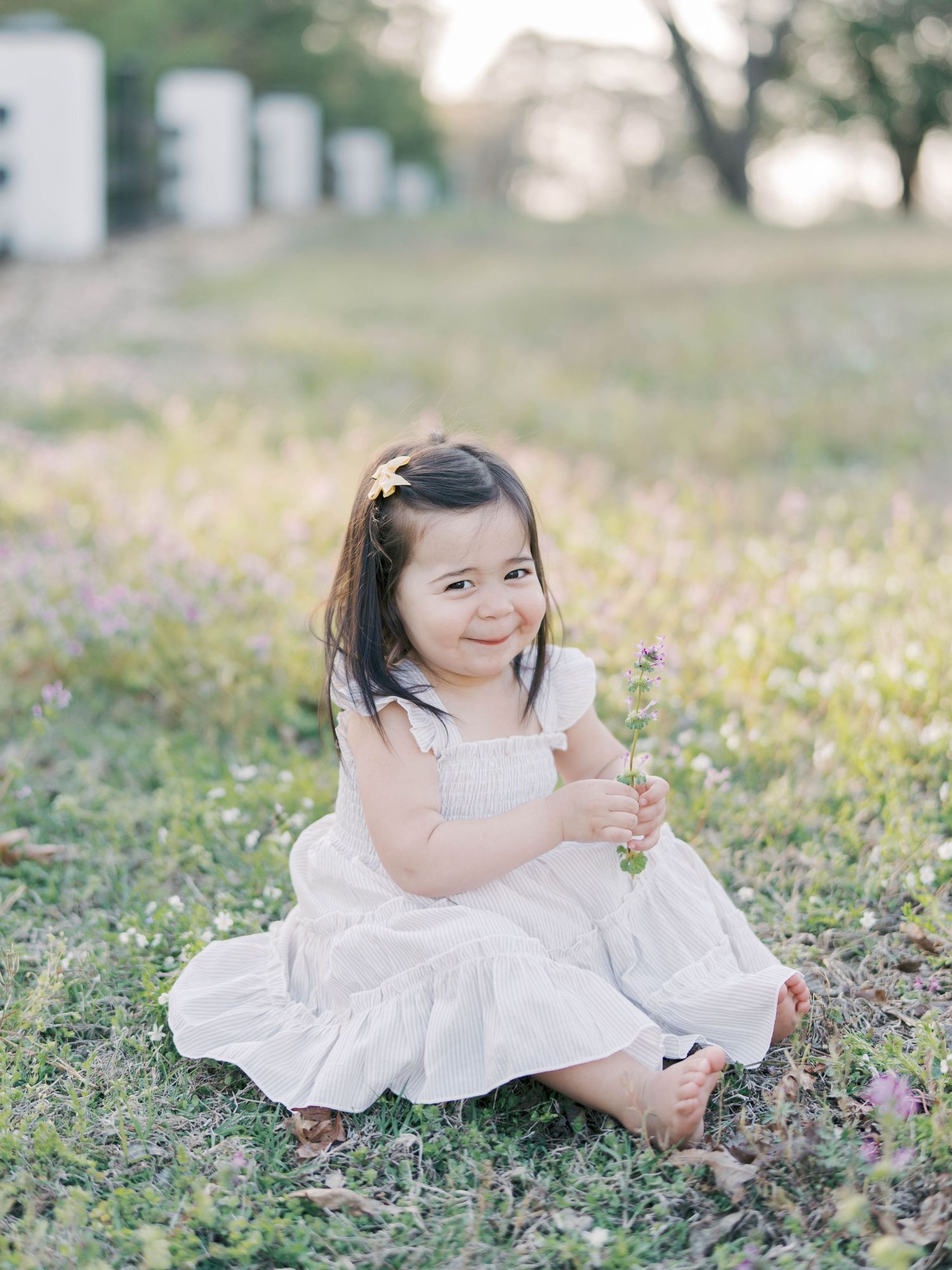 Young girl in white dress sits in flowering field holding wildflowers.